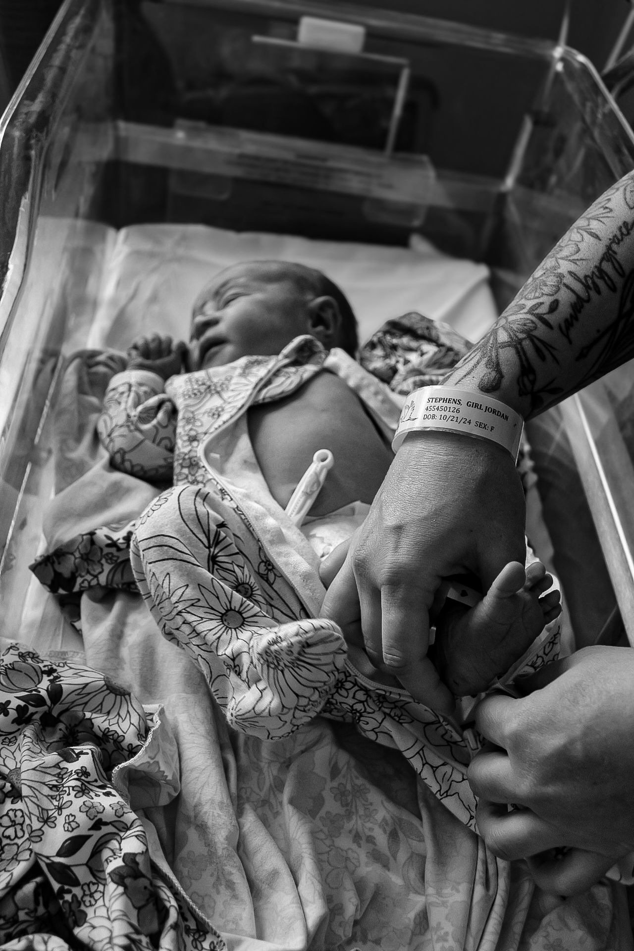 Hospital scene showing gentle hands caring for a sleeping newborn wrapped in floral fabric.