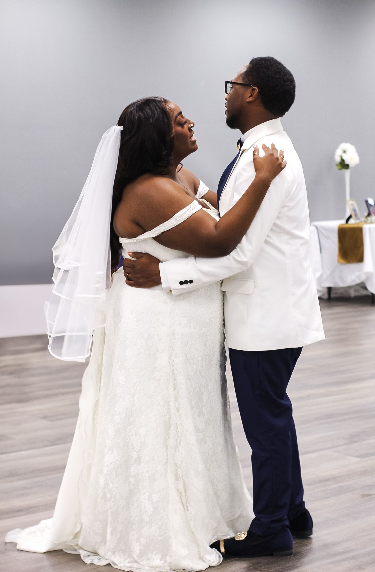 Joyful couple sharing first dance in white wedding attire on dance floor.