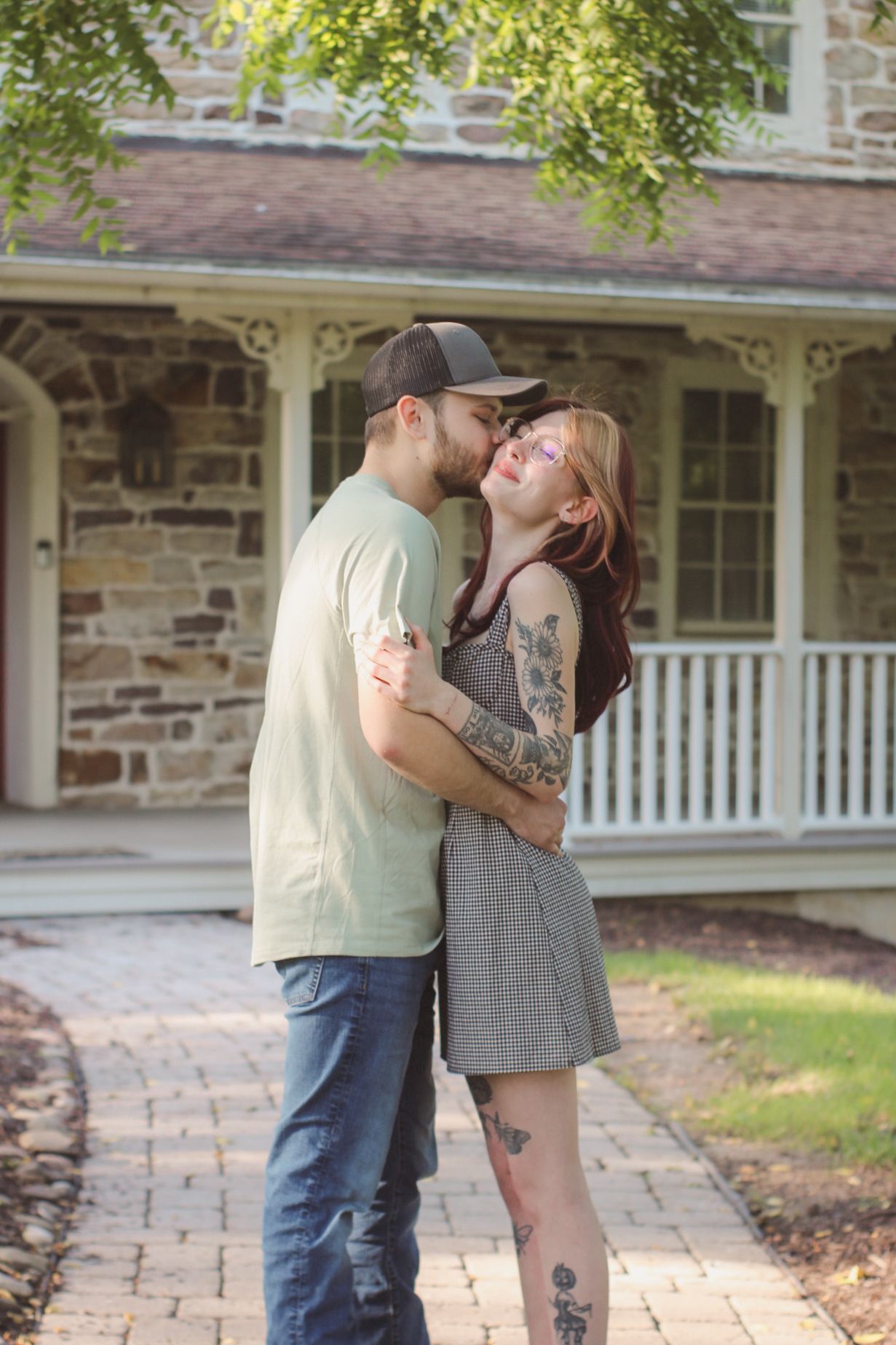 Romantic couple embracing in front of a rustic stone building with white porch.