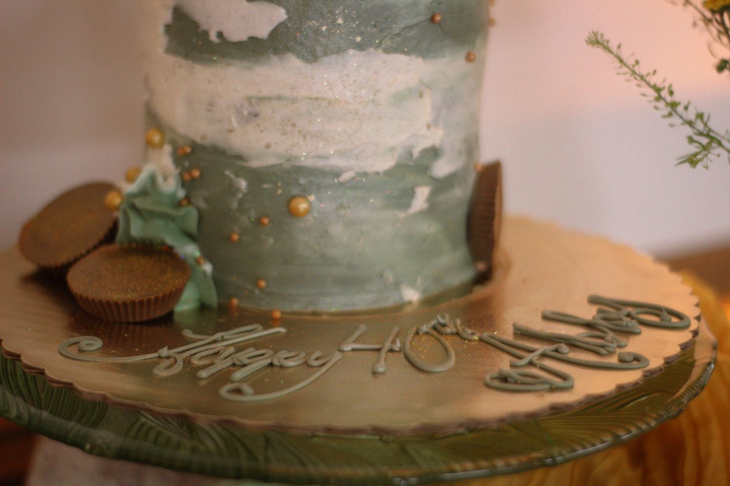 A sage green decorated cake with chocolate cookies displayed on a cake stand.