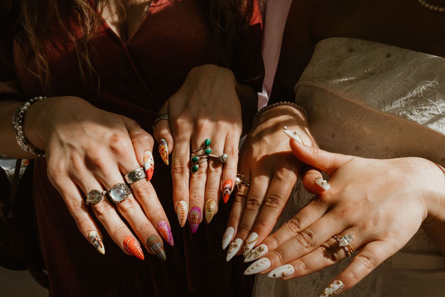 Multiple hands displaying colorful nail art and stacked rings with gemstones, showcasing boho jewelry and manicure styles.