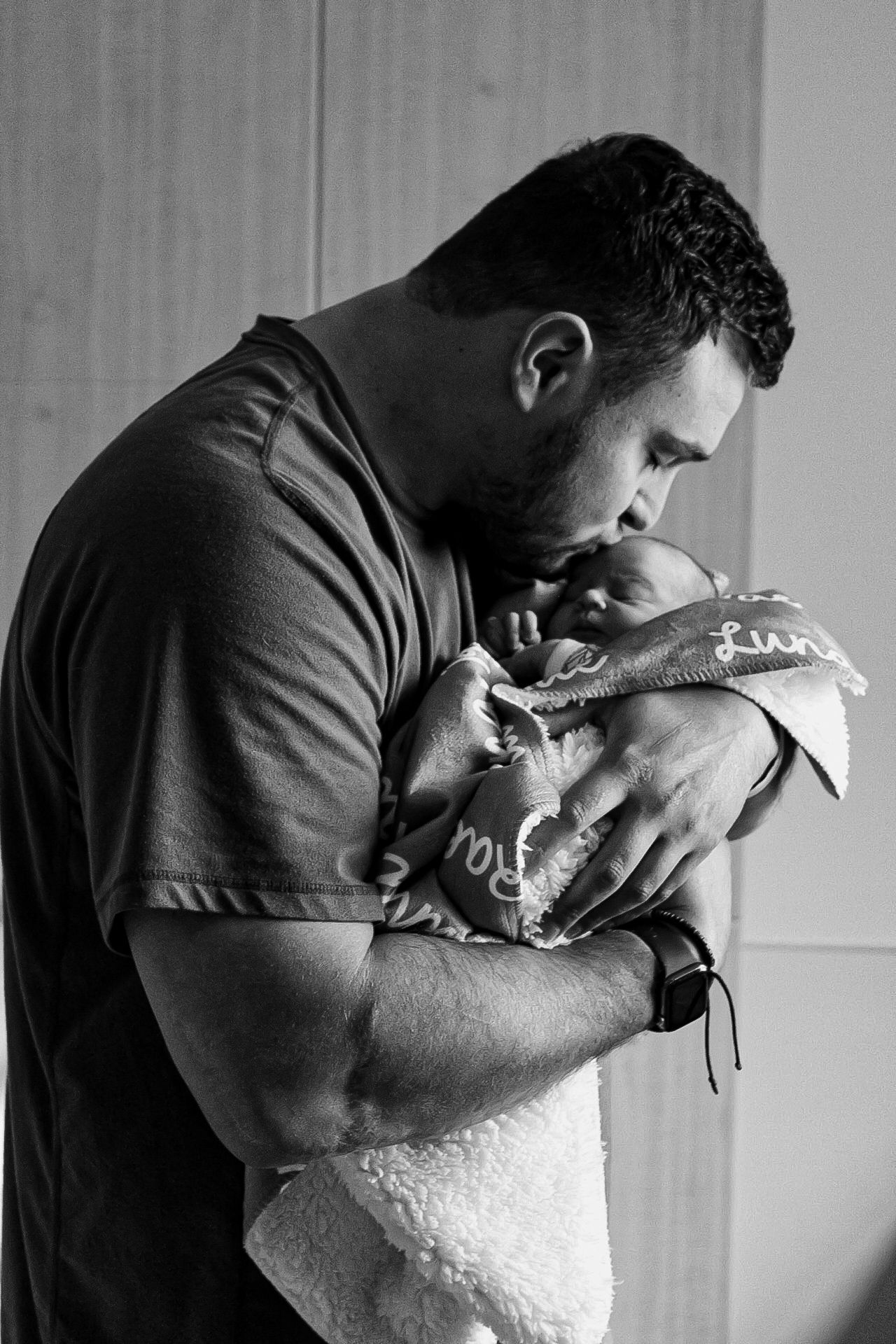 Intimate black and white portrait showing a gentle embrace between parent and newborn.