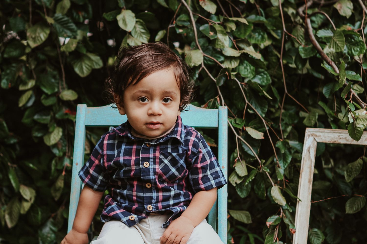 Child in checkered shirt and white pants sitting on turquoise chair.