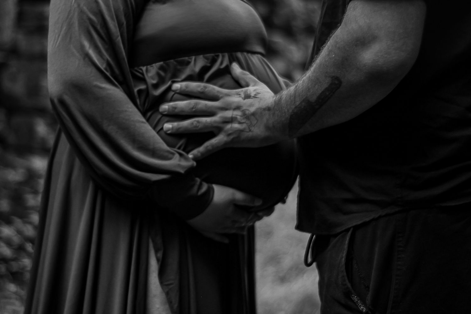 A black and white intimate moment capturing hands cradling a pregnant belly.