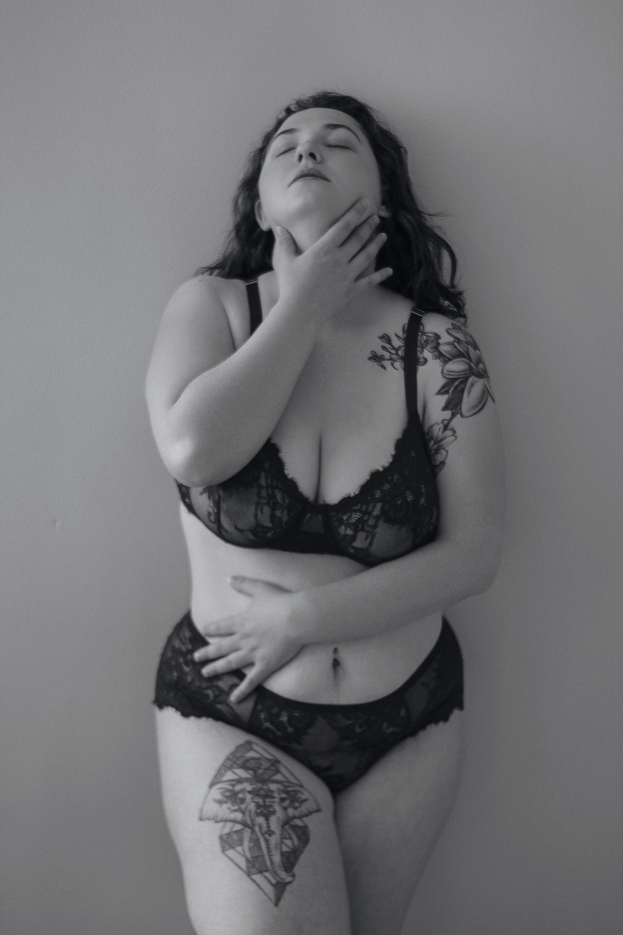 Artful black and white boudoir photoshoot featuring lace lingerie and sensual poses against neutral background.