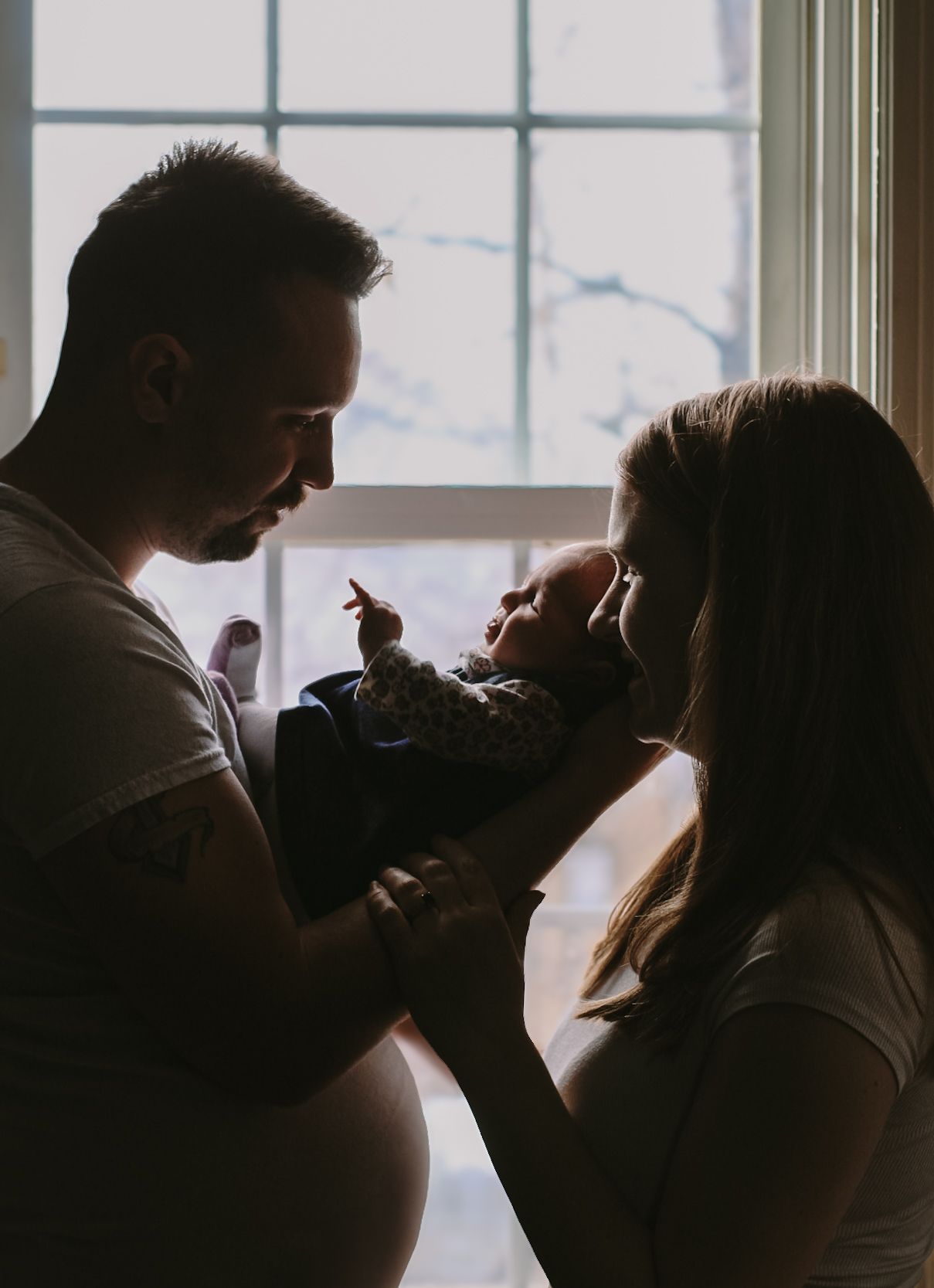 A silhouetted family shares a tender moment by a bright window.
