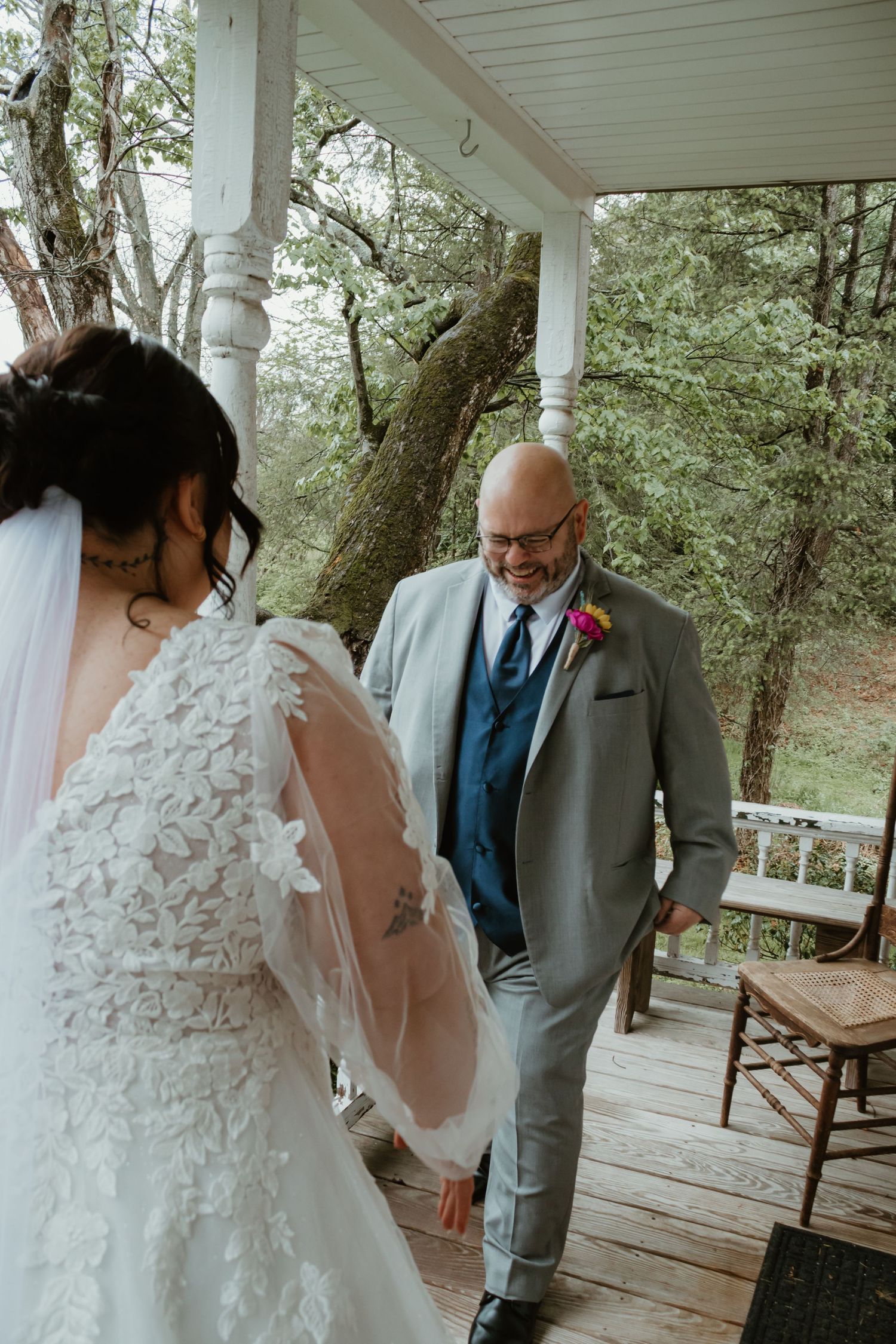 Father sees bride in wedding dress for first look on rustic porch, emotional reaction captured outdoors.