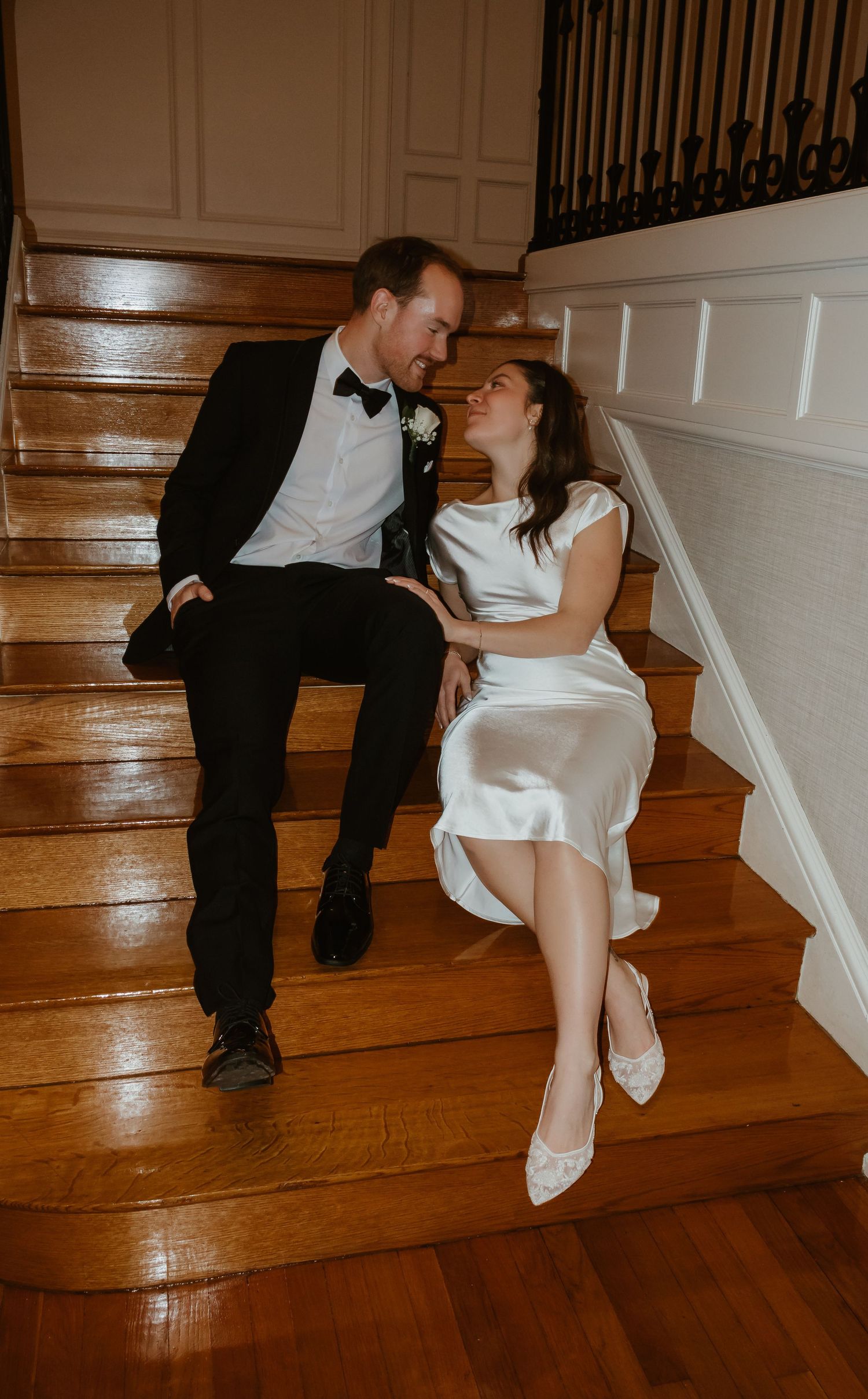 Bride and groom sitting on wooden staircase, sharing a romantic moment in wedding attire.