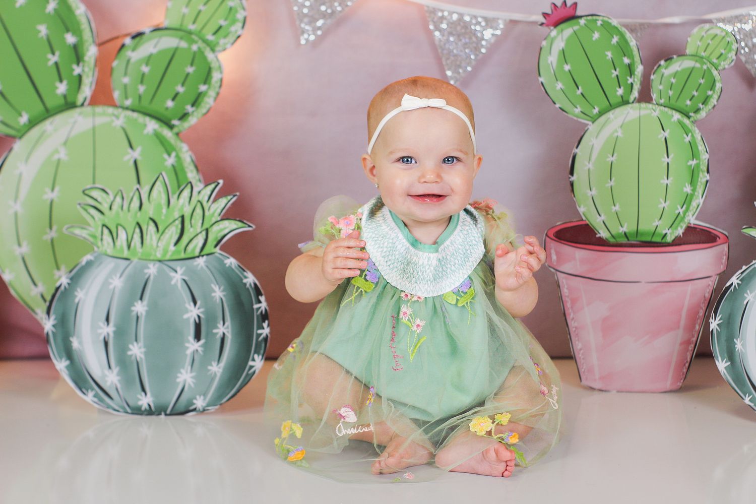 Sweet cactus-themed photography setup featuring decorative potted plants and festive string lights.