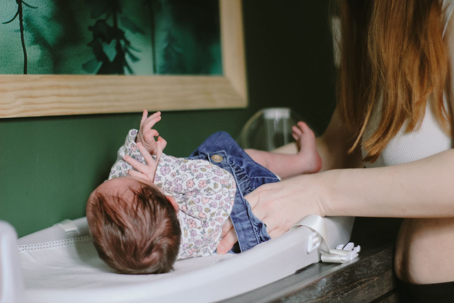 A gentle diaper change moment captured near a green wall.