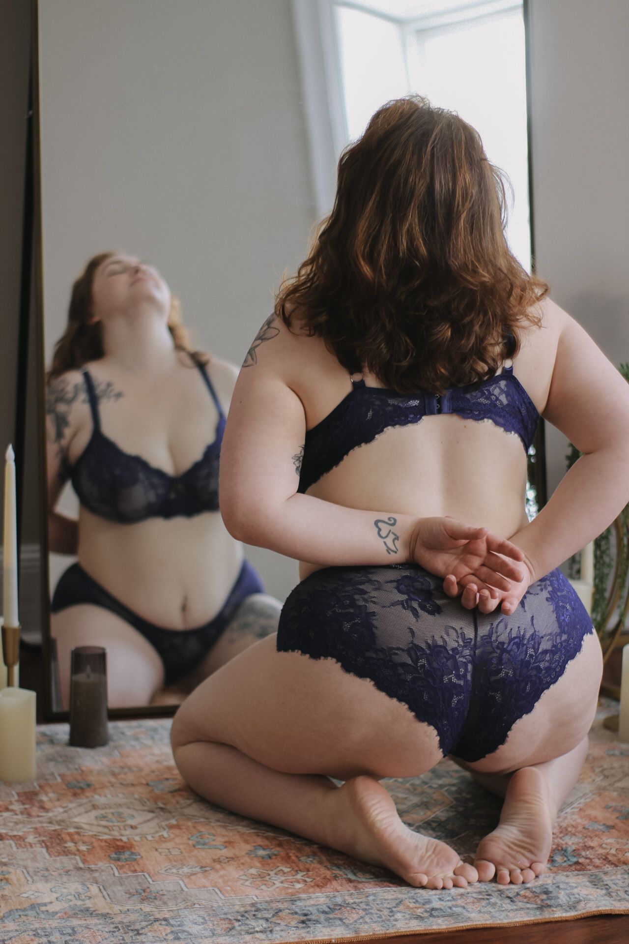 Artistic boudoir photos on floral rug featuring navy lace lingerie and natural lighting.