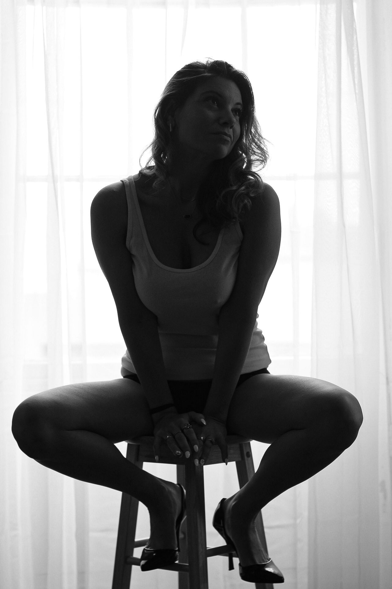 Silhouette photo of person seated on stool by window in athletic wear.