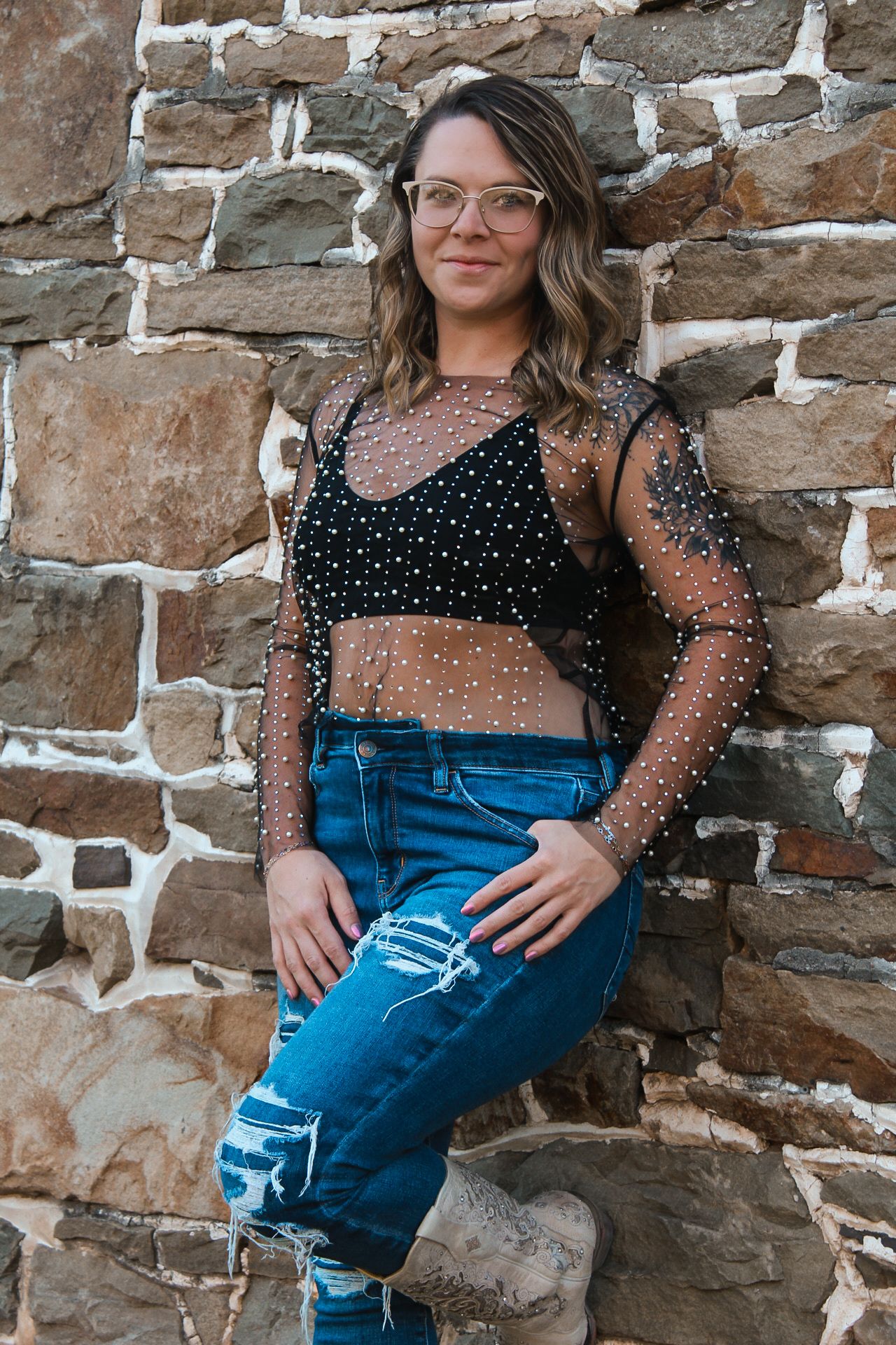 Trendy outfit featuring a sheer polka dot mesh top paired with distressed jeans against a stone wall.