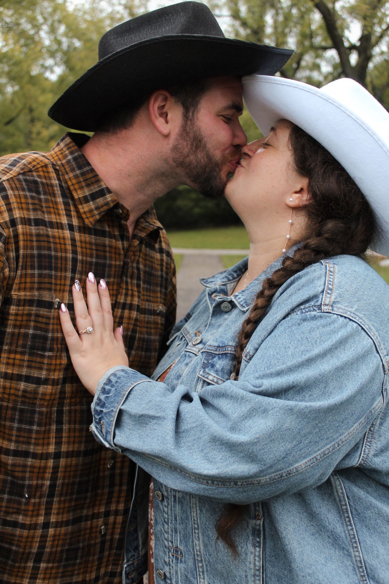 A romantic moment between a couple in cowboy hats and casual western wear in an outdoor setting.