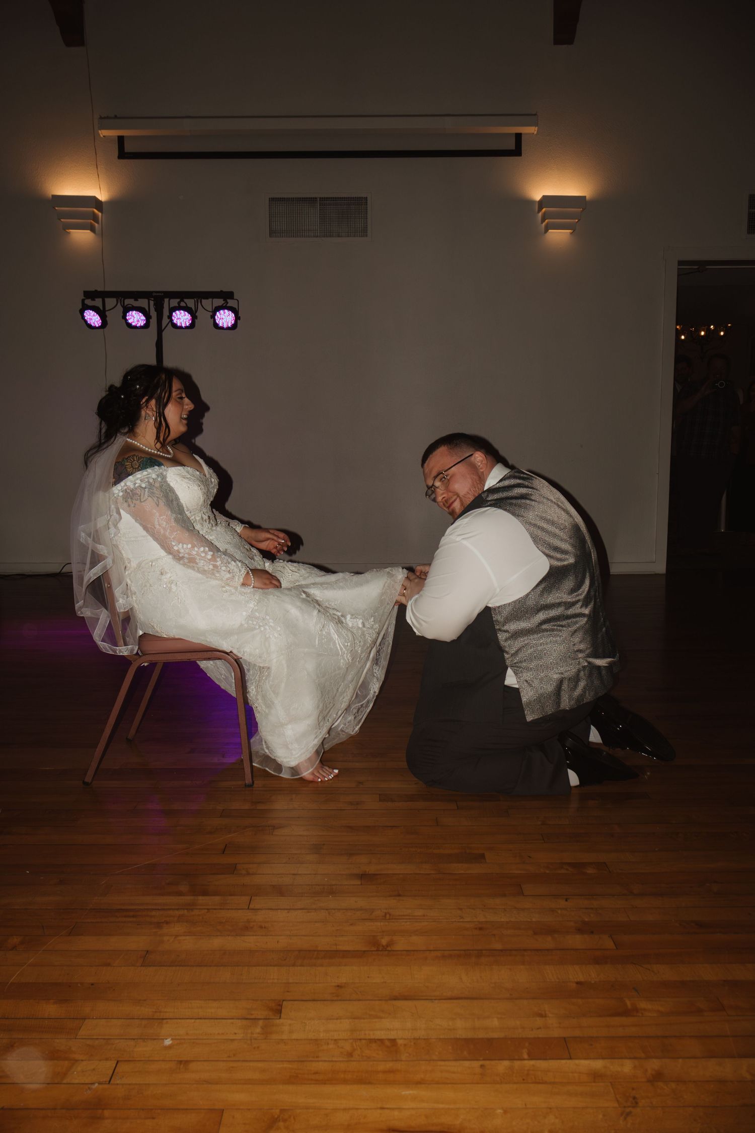 Groom kneeling on dance floor removing bride's garter during wedding reception in elegant venue.