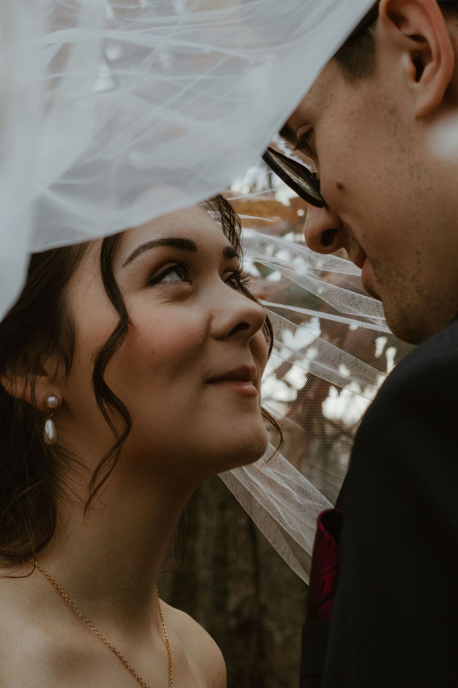 Romantic close-up of a couple sharing an intimate moment under a delicate white veil in natural light.