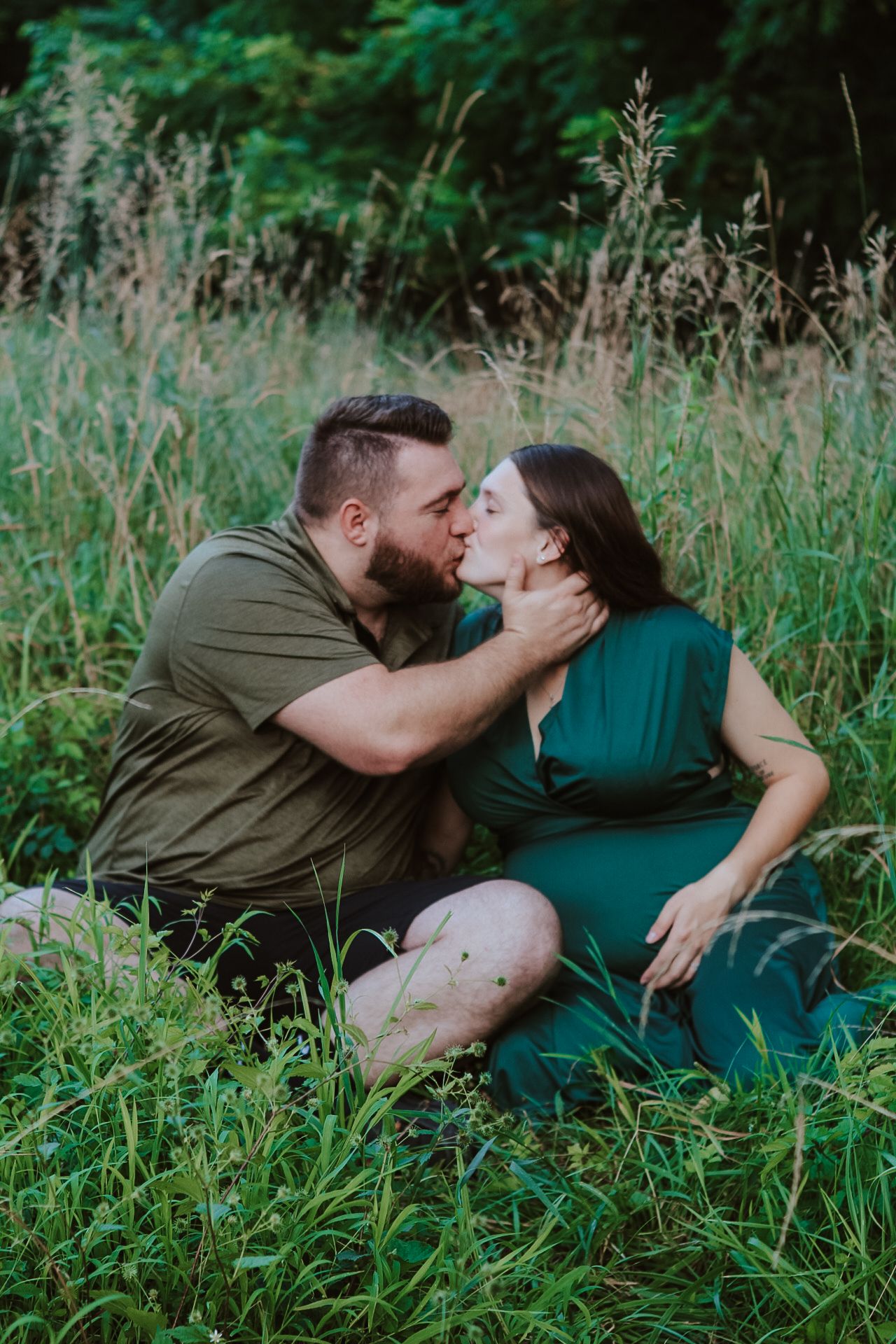 Intimate maternity photo session in tall grass with couple sharing romantic moment.
