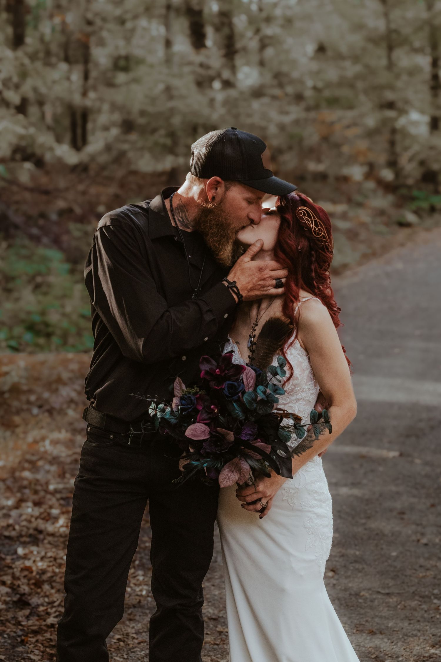 A couple in wedding attire shares a romantic kiss on a wooded path during their autumn wedding celebration.