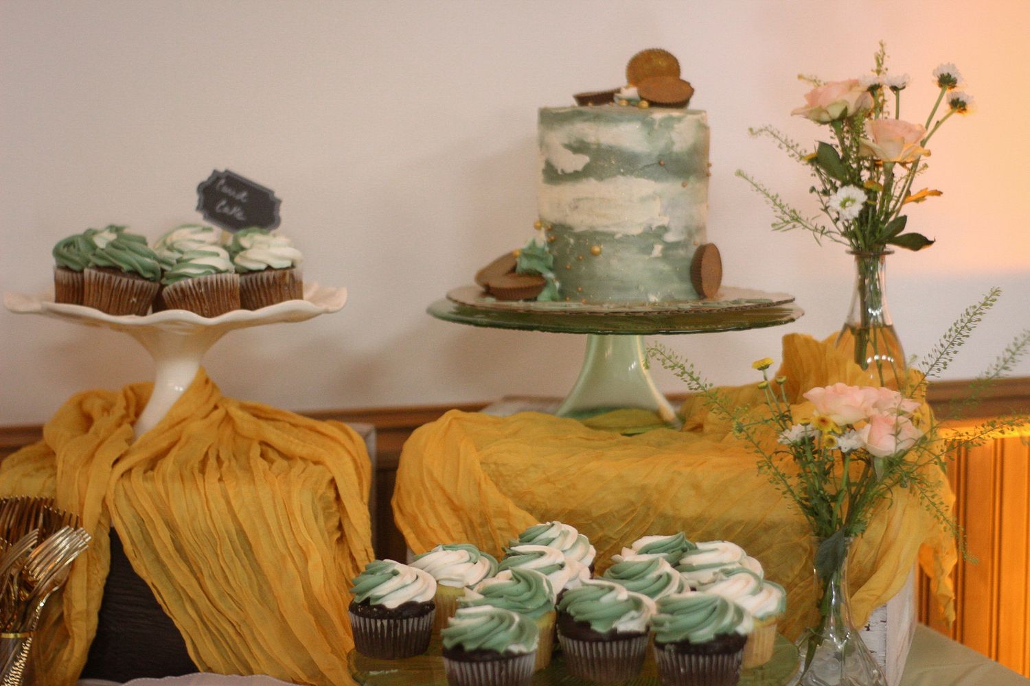 Dessert table with mint green cake, cupcakes and yellow fabric decor.