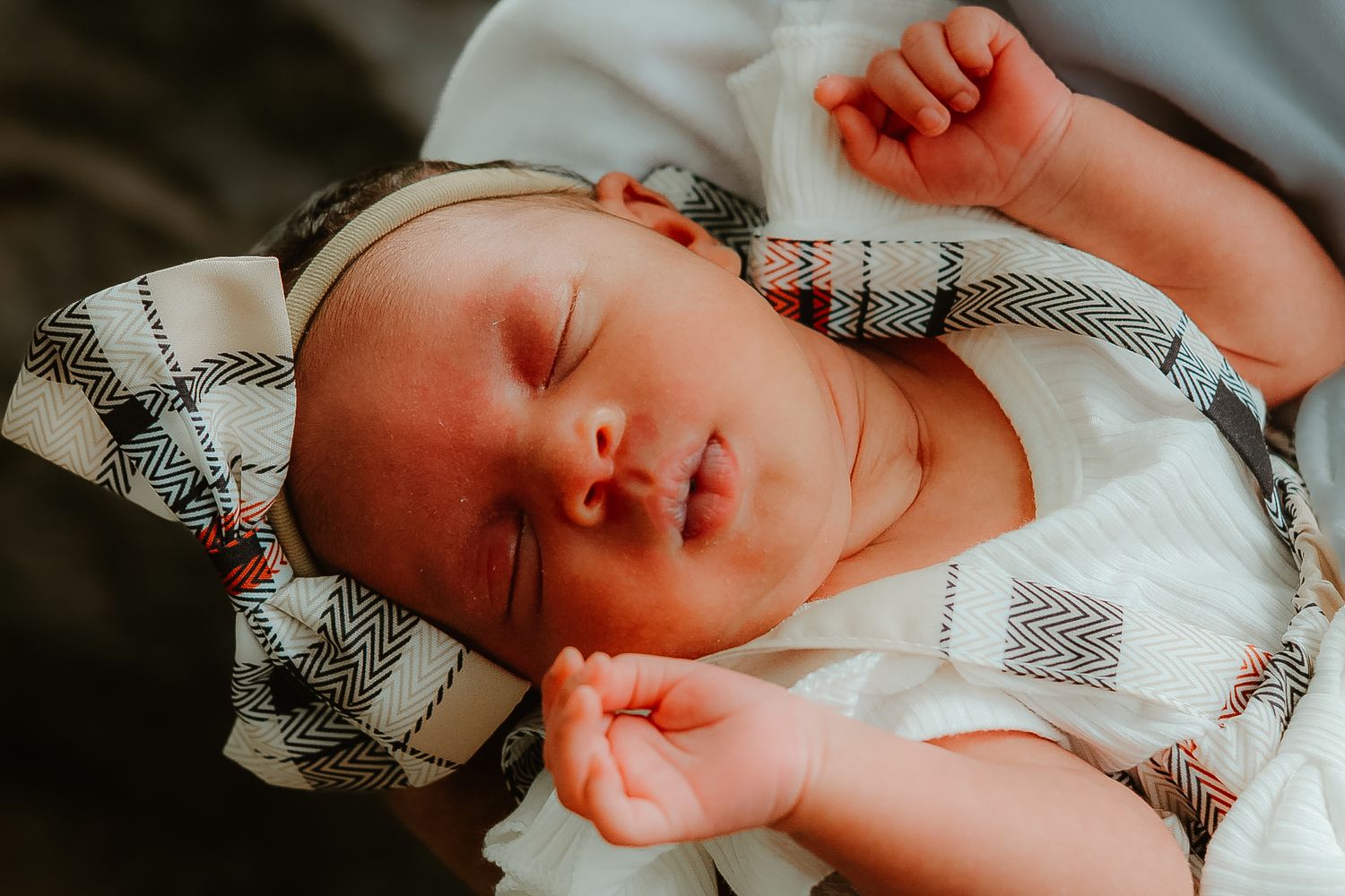 A newborn baby sleeps peacefully while wrapped in a cozy striped blanket.