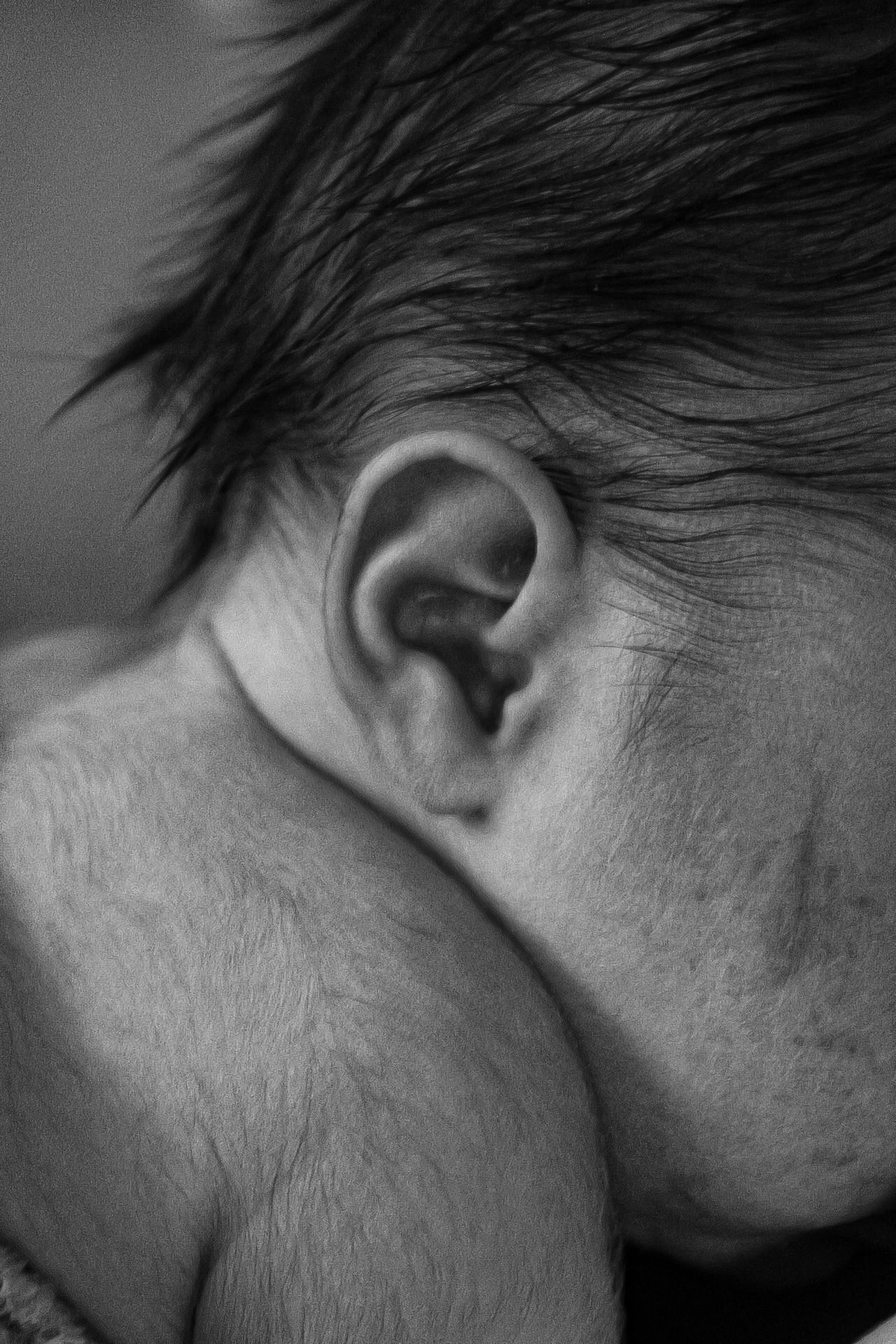 Close-up black and white photo of a baby's ear and hair.