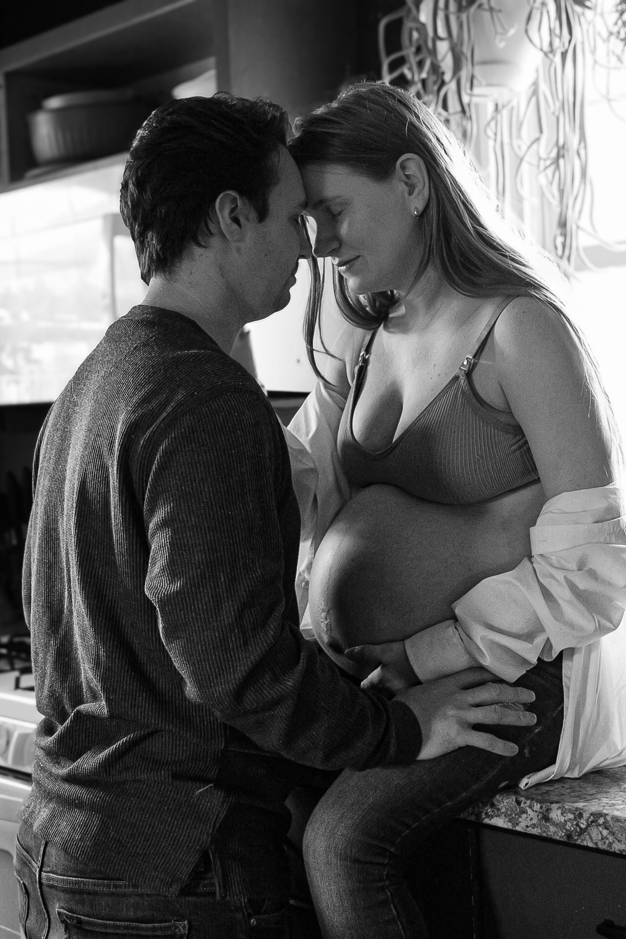 An intimate black and white portrait of an expectant couple sharing a tender moment.