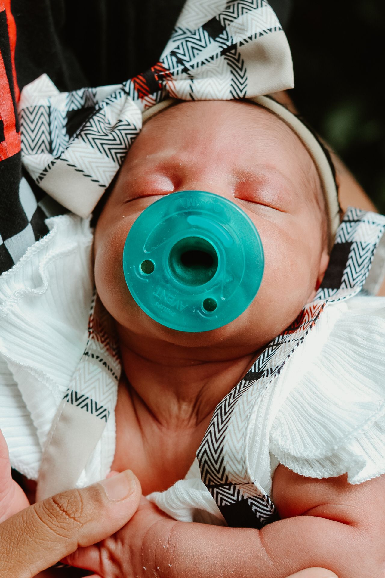 A sequence of close-up shots showing a teal pacifier placed in an infant's mouth with chevron print fabric in view.