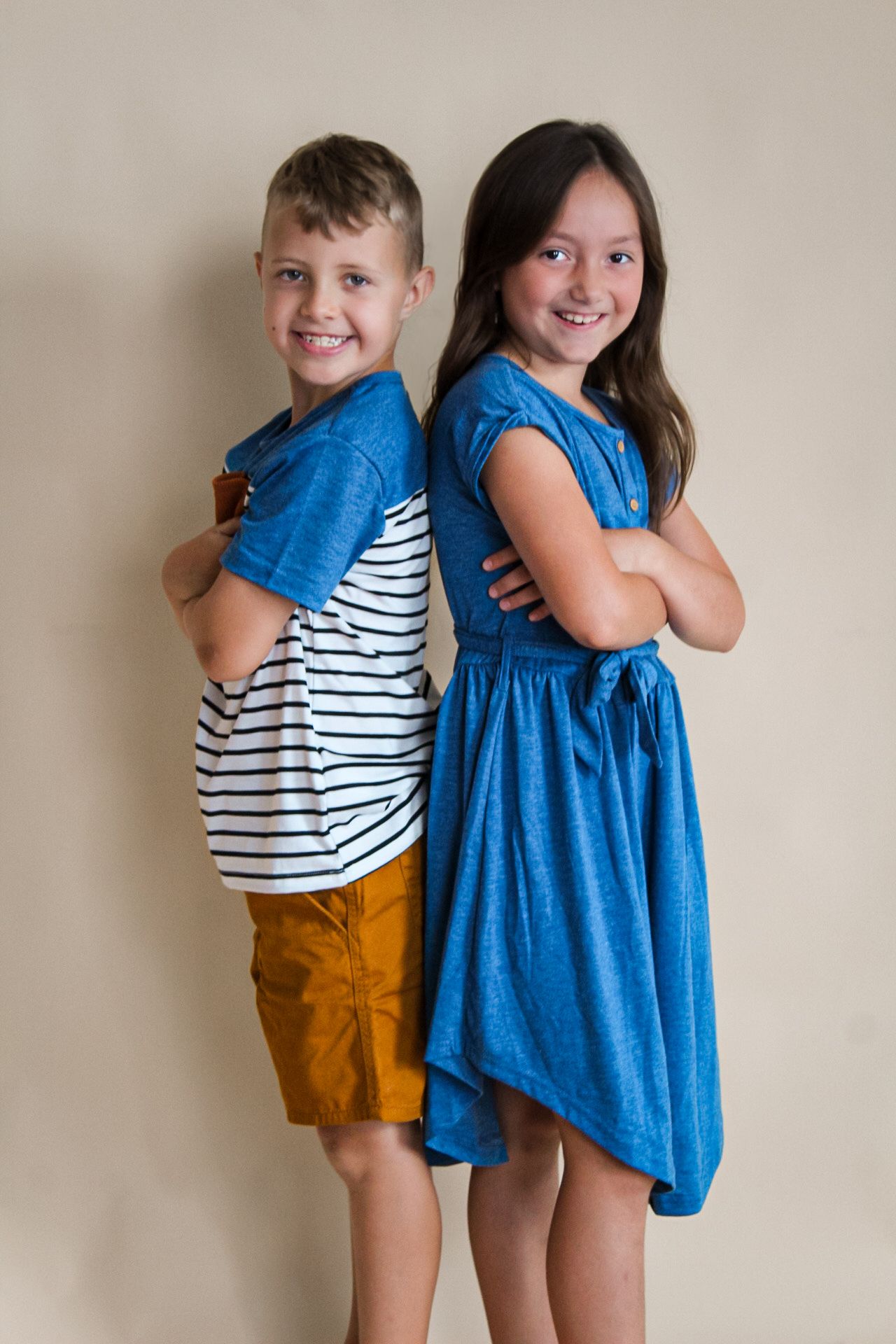 Two children in blue dress and striped shirt posing playfully against neutral studio background.