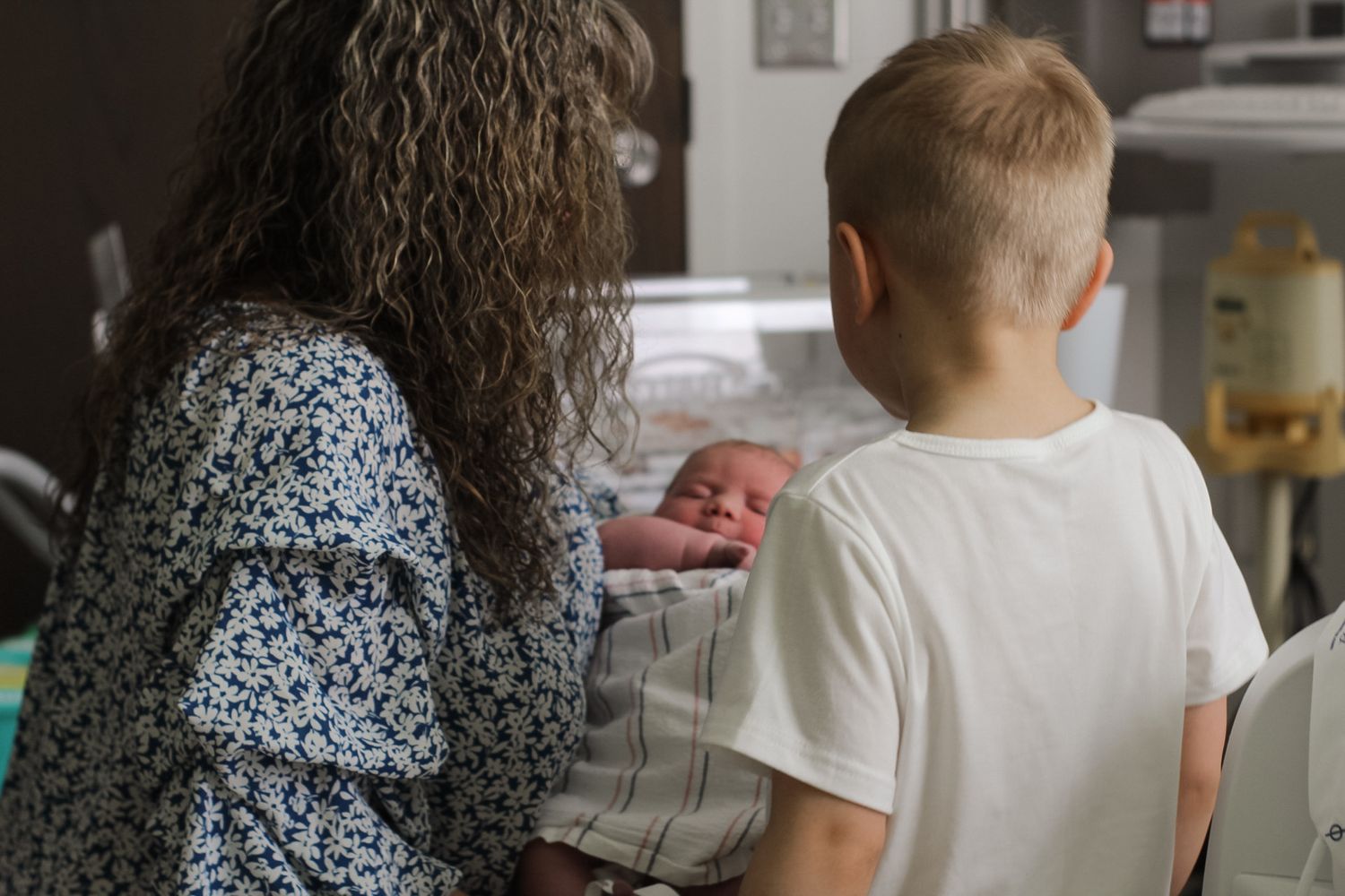Hospital room scene showing people gathered around a medical bassinet.
