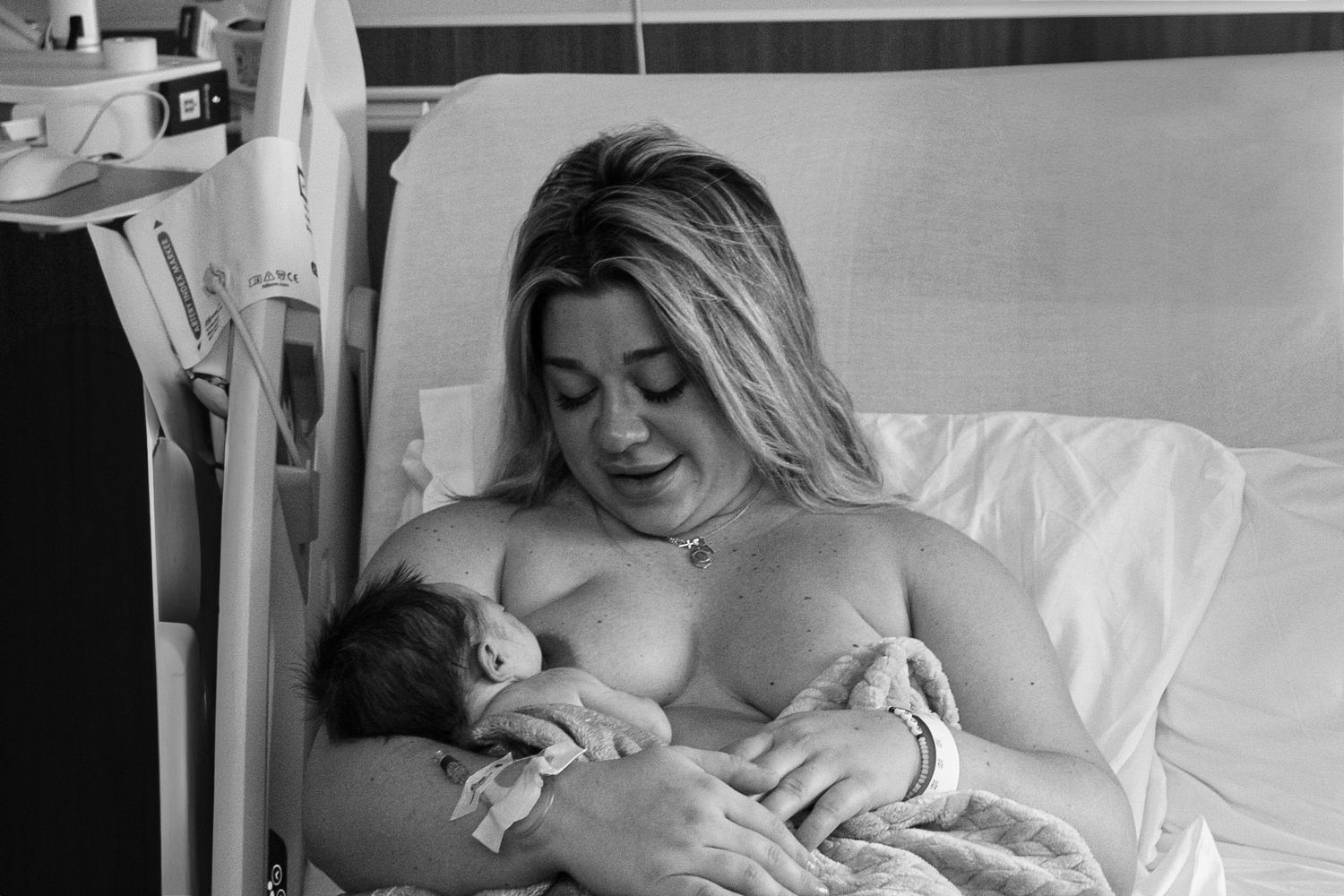Black and white image of a new mother breastfeeding her newborn baby in a hospital bed.