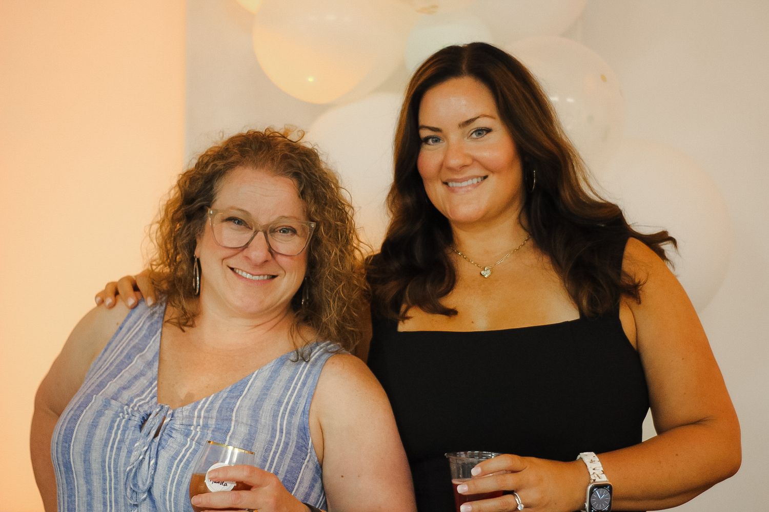 Two friends sharing a joyful moment at a celebration wearing blue and black dresses.