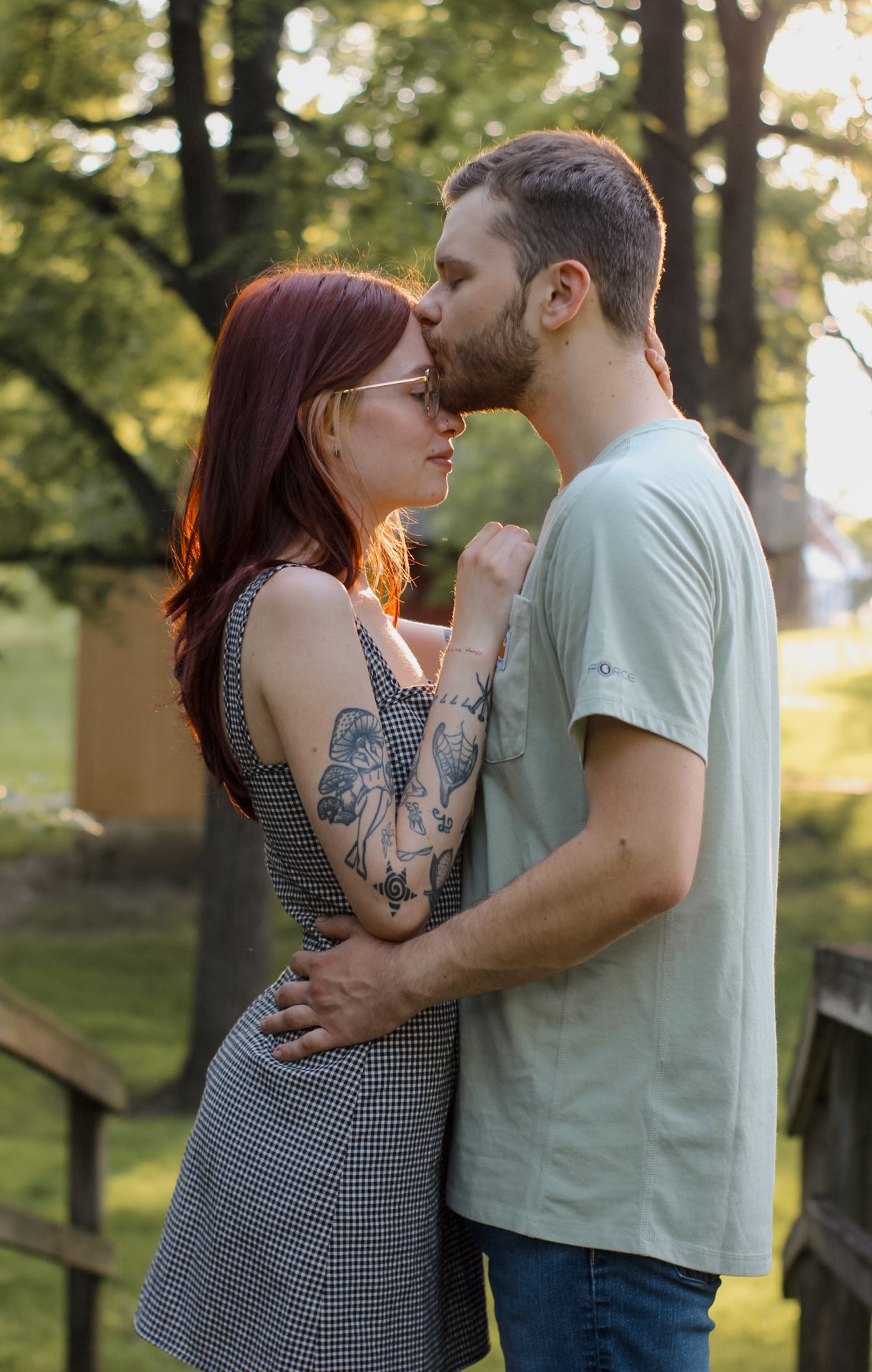 Couple in casual attire sharing tender moments outdoors in warm evening light.