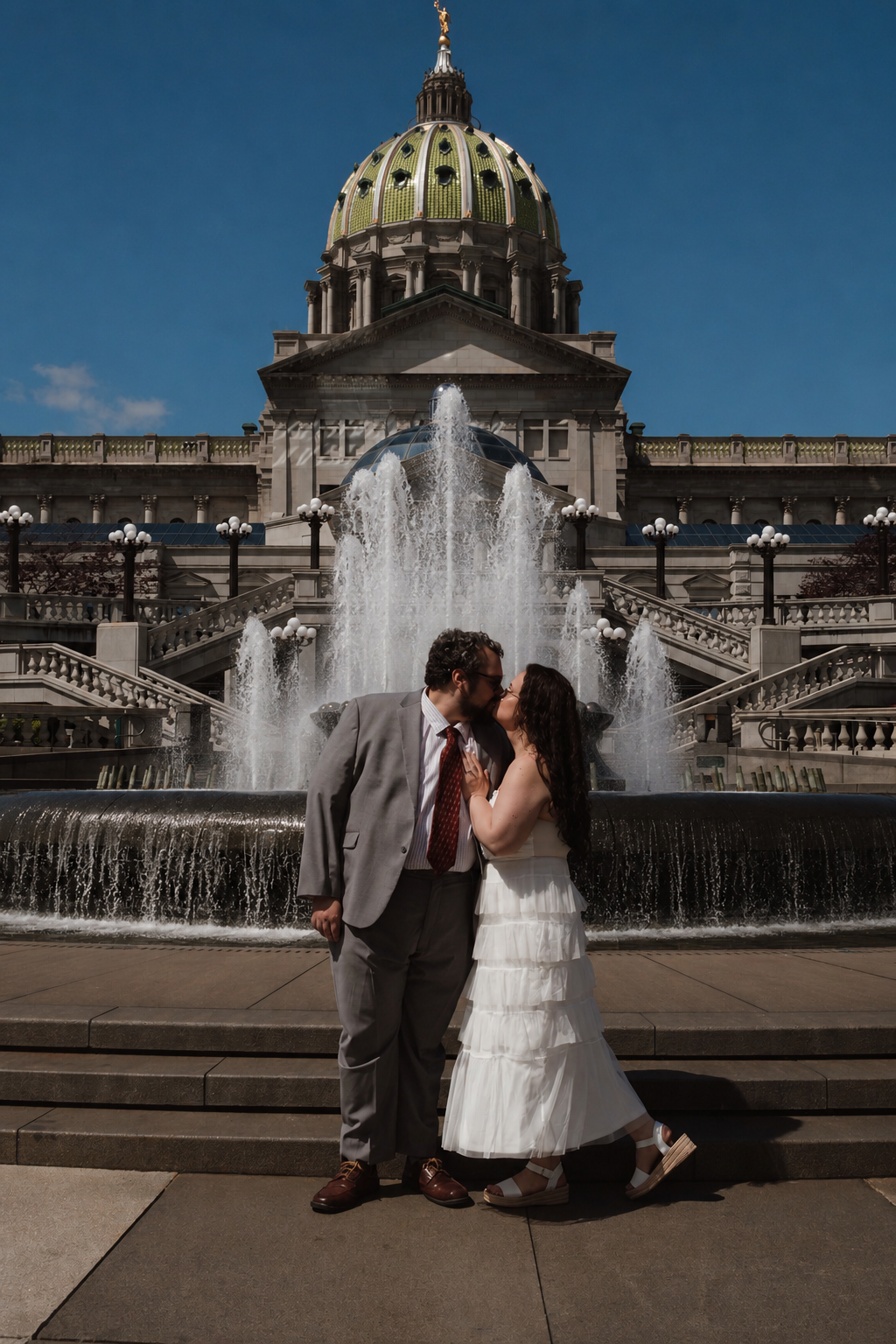Newlywed couple kissing in front of Pennsylvania State Capitol fountain on their wedding day.