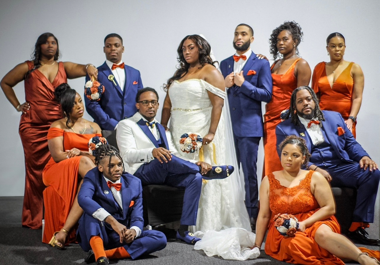 Wedding party photo with bridesmaids in orange and groomsmen in navy suits.