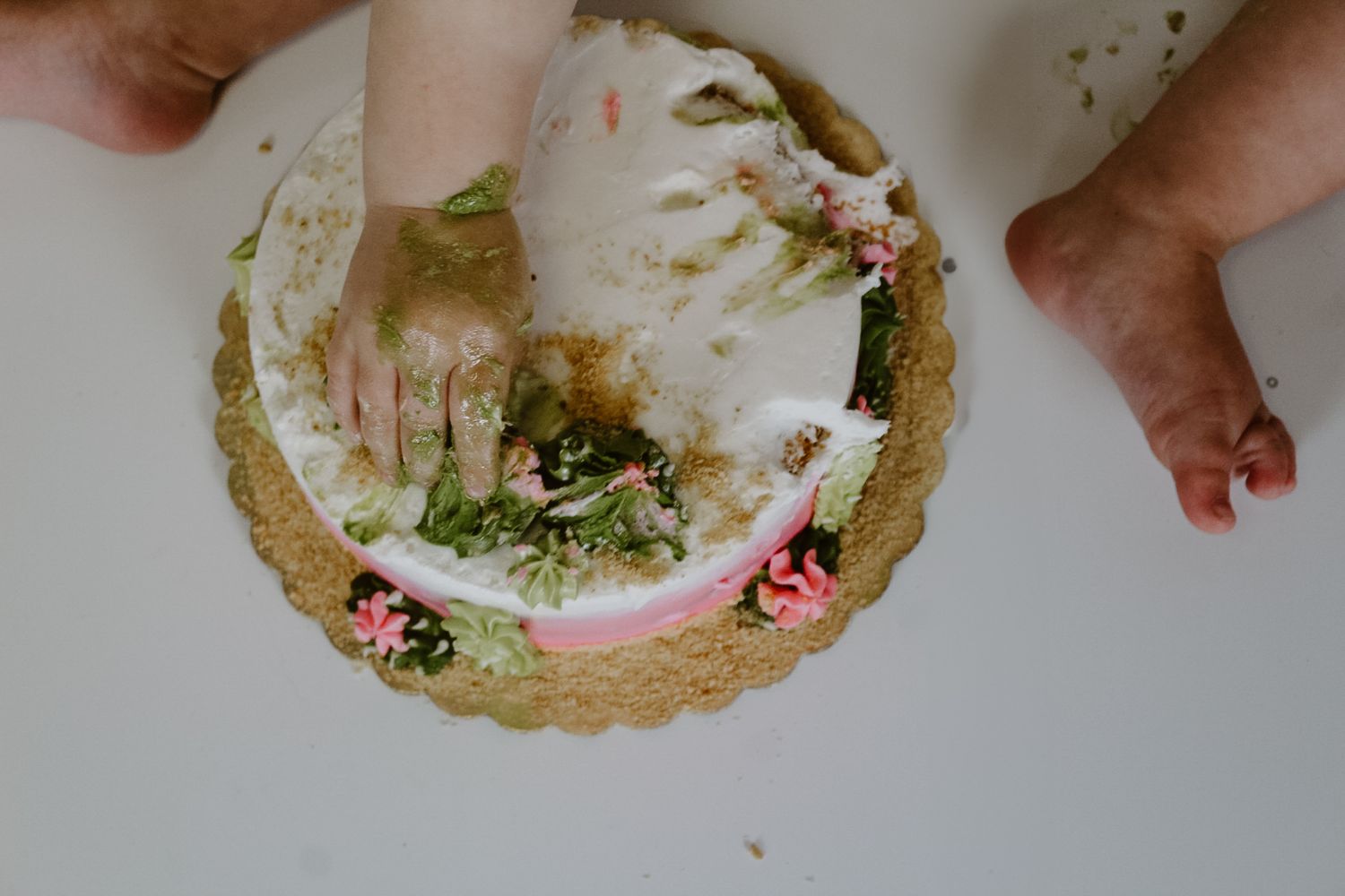 Smashed birthday cake showing green and pink frosting remnants on gold cake board.