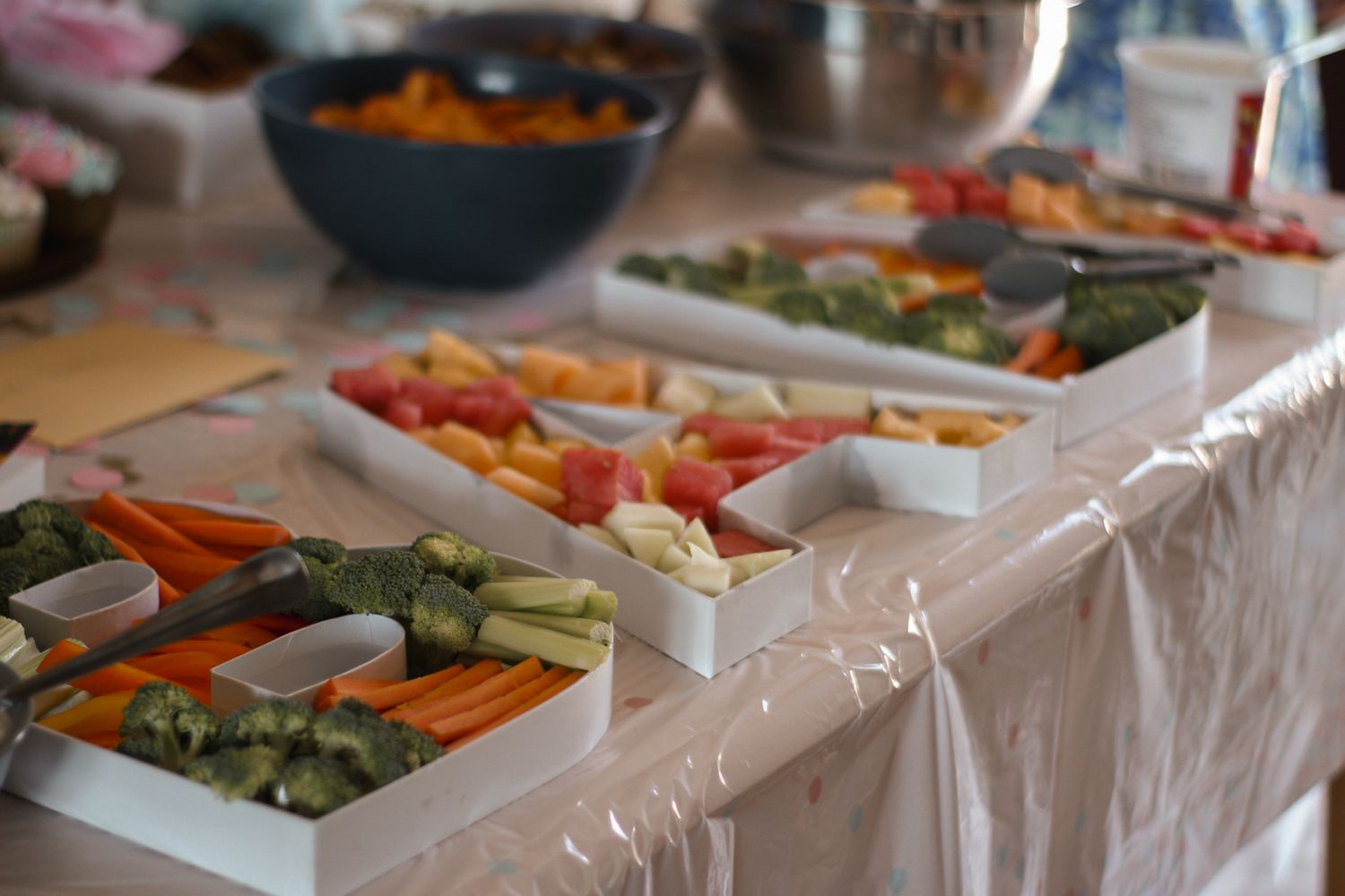 Long table with fresh vegetable and crudité platter spread on white tablecloth.