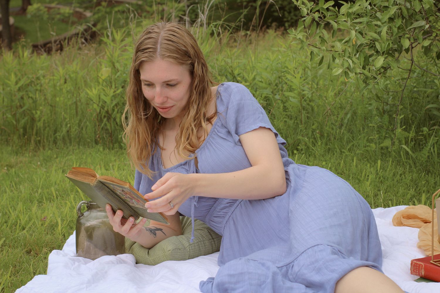 Woman in a blue dress enjoys a picnic on a white blanket with lanterns and old vintage books. Cottage core vibes