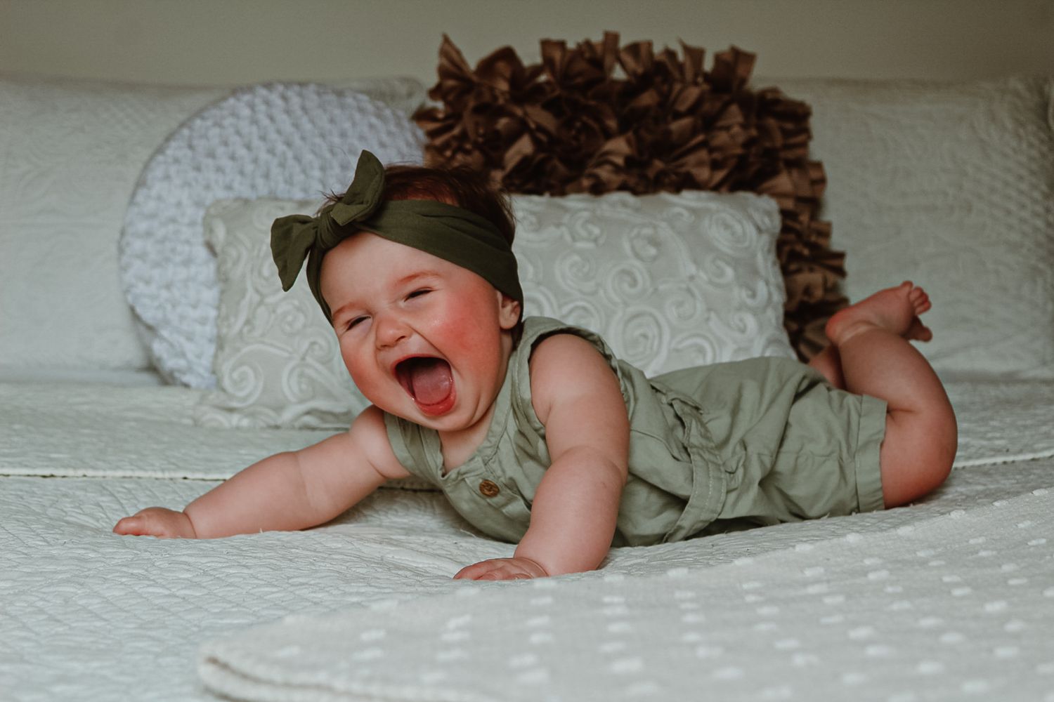 Baby lying on white textured bedding with curly hair and playful expressions.