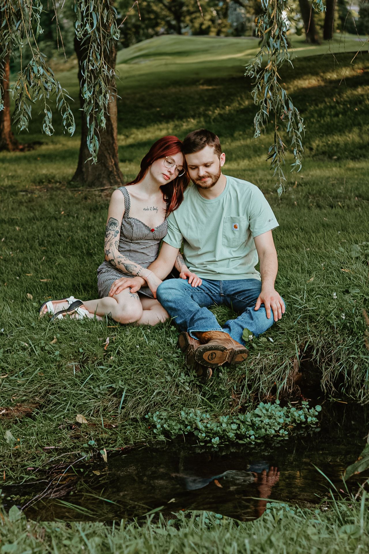 Couple sitting by a peaceful pond under weeping willow trees.