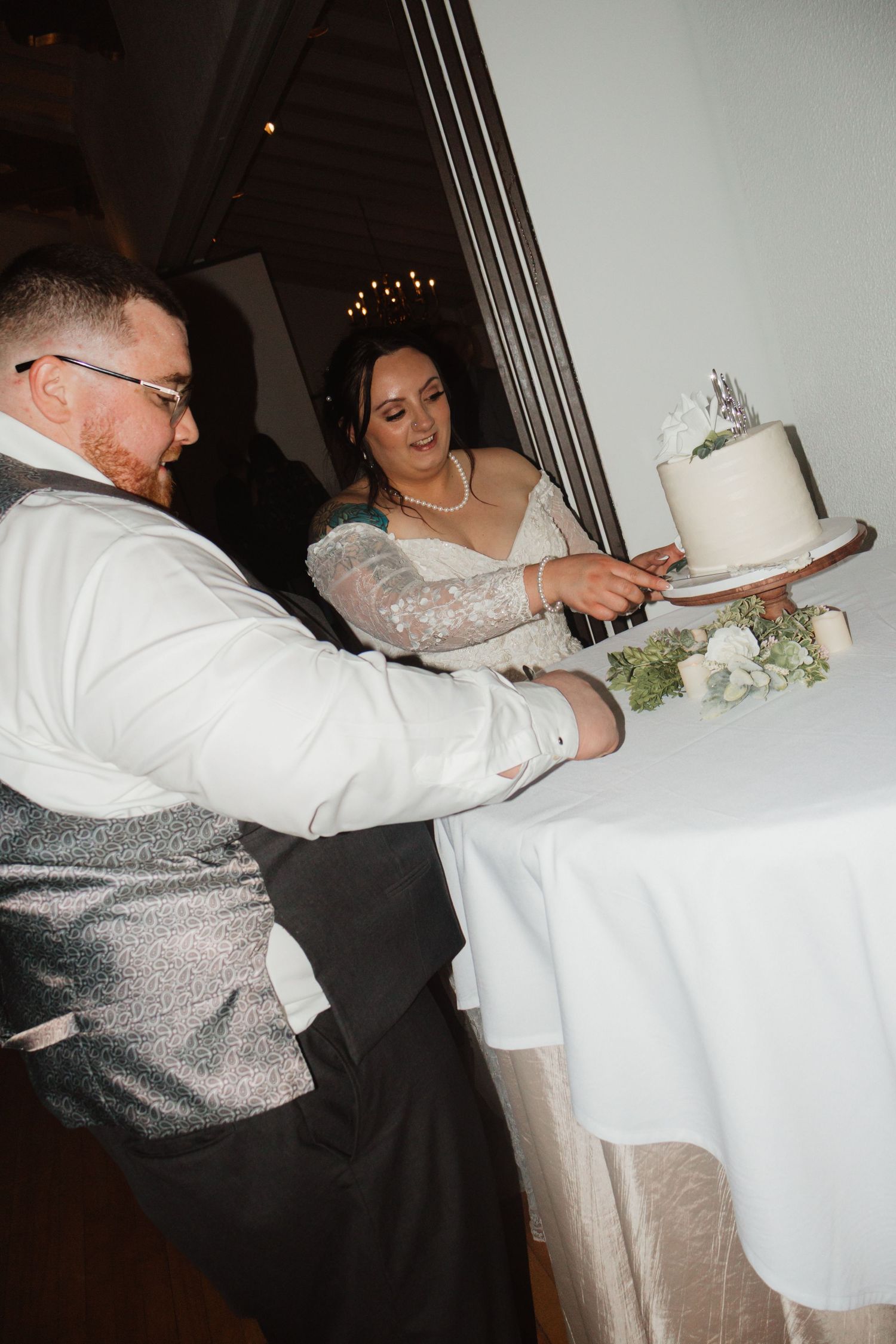 Bride and groom cutting their white wedding cake together at their reception venue.