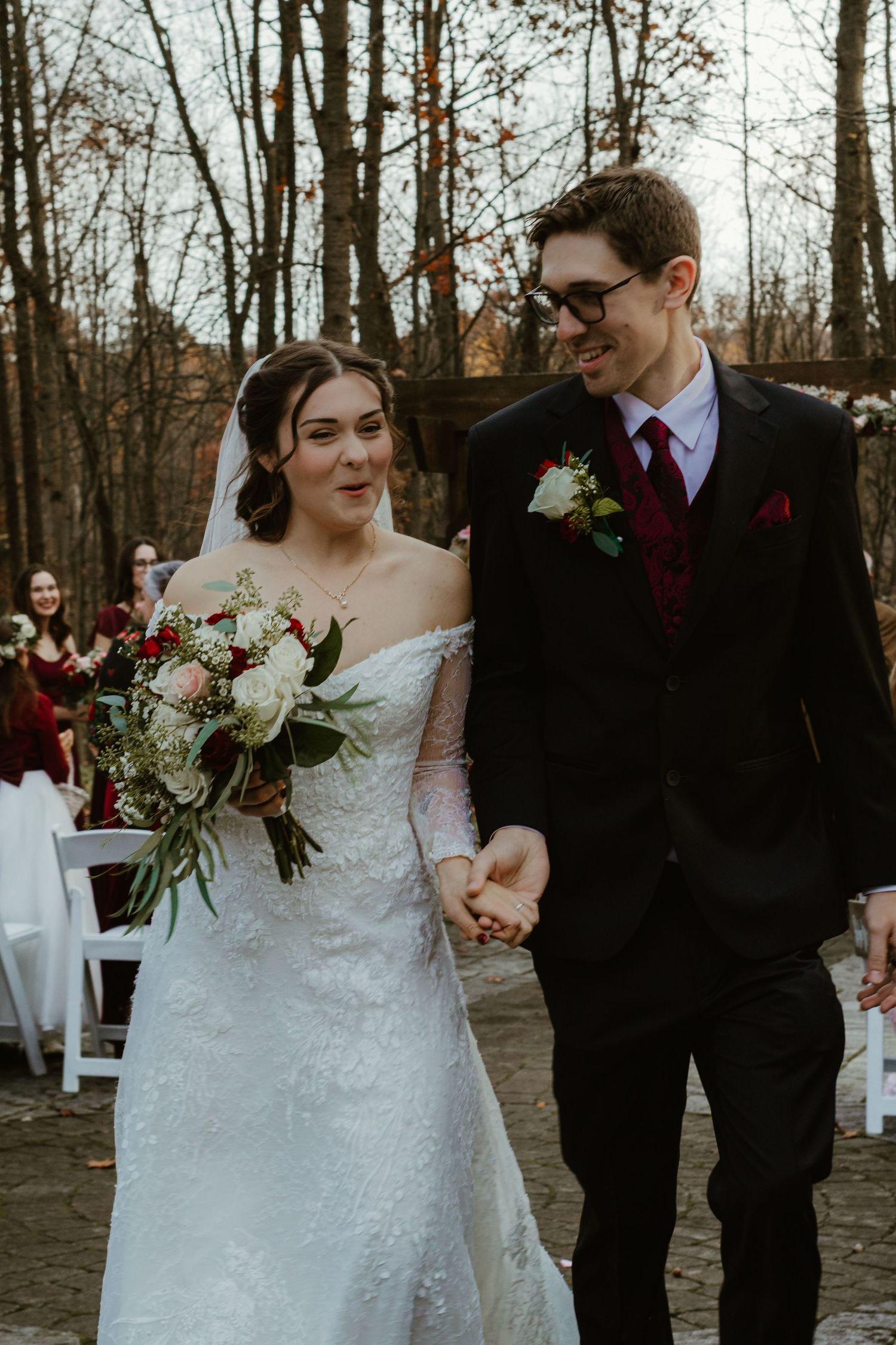 A couple shares a joyful moment at their outdoor autumn wedding ceremony surrounded by bare trees and white chairs.