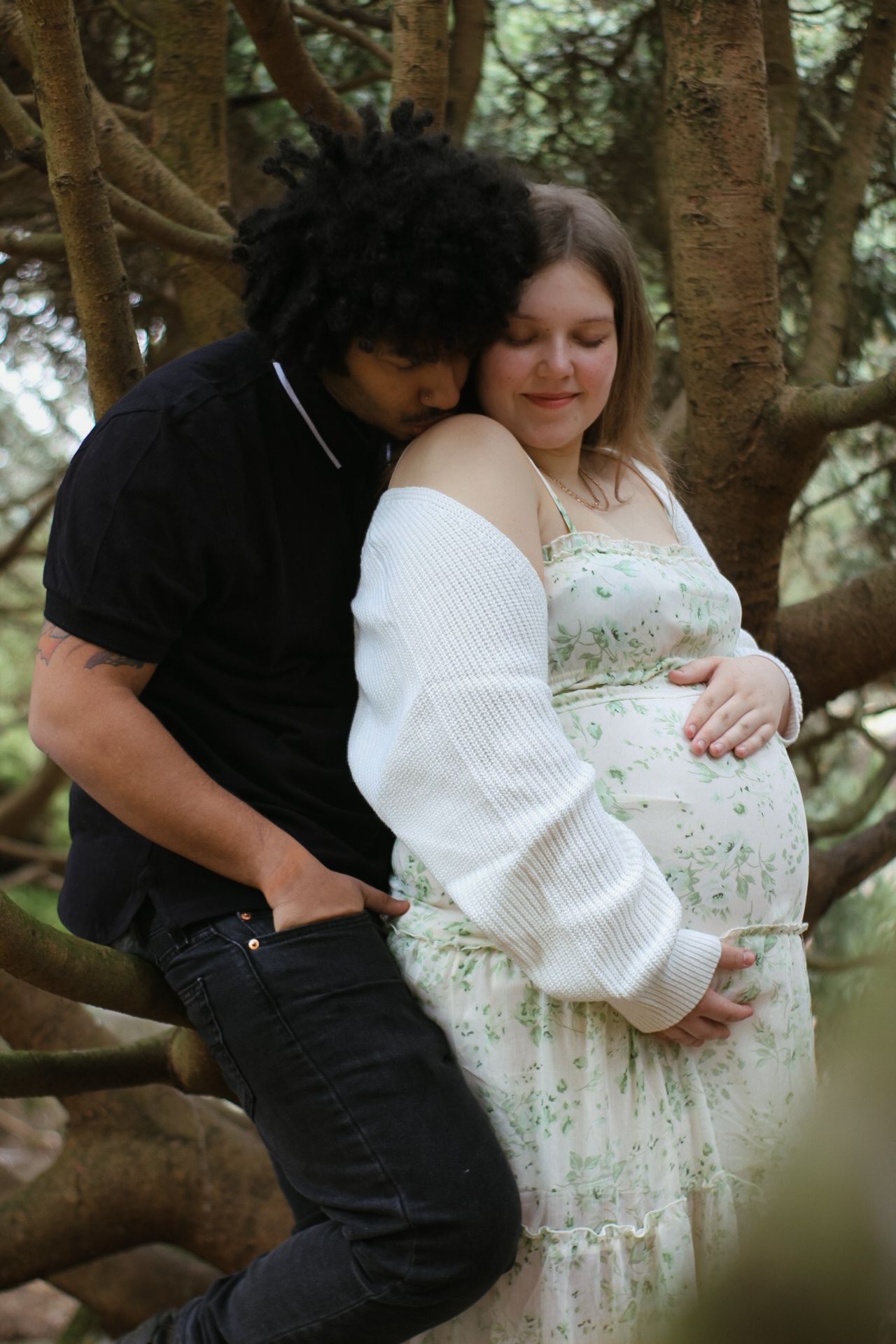 A tender maternity moment captured between a couple in a wooded setting.