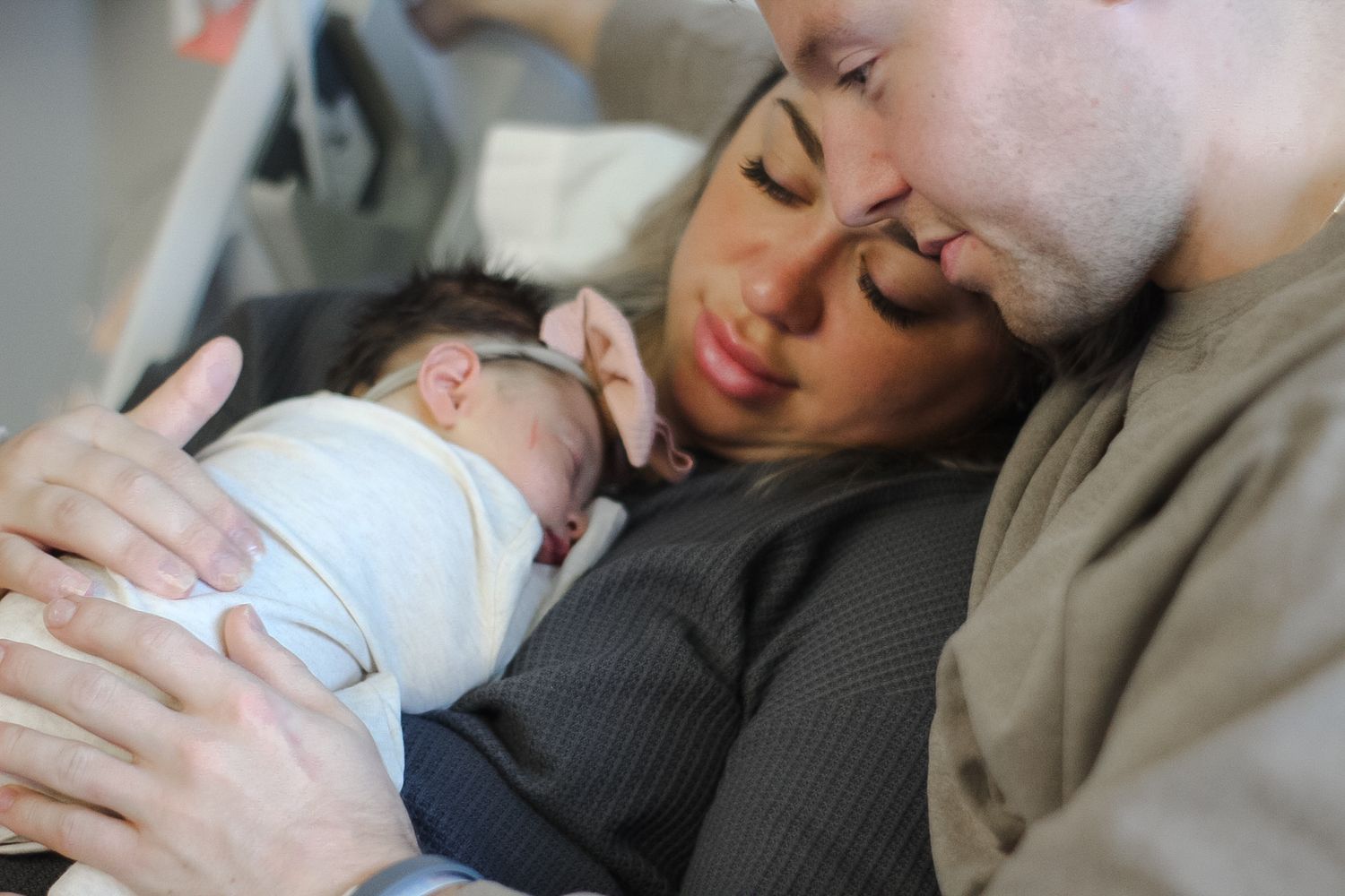 Intimate black and white photo of parents cradling their sleeping newborn baby.
