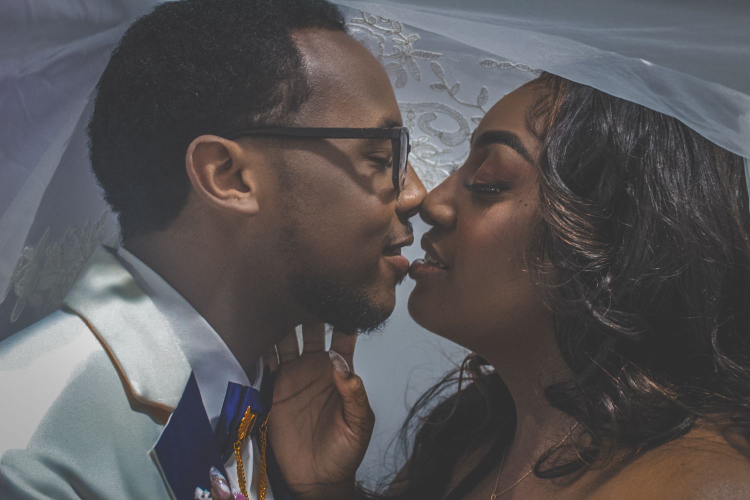 Intimate wedding portrait under a veil showing a romantic almost-kiss moment.