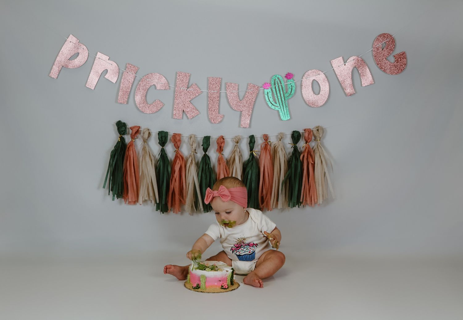 A first birthday celebration setup with pink and green tissue paper tassels and a cake smash scene.