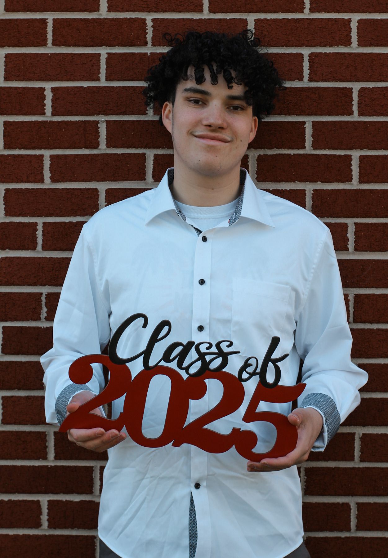 Three people in white shirts holding red Class of 2025 letters against brick wall.