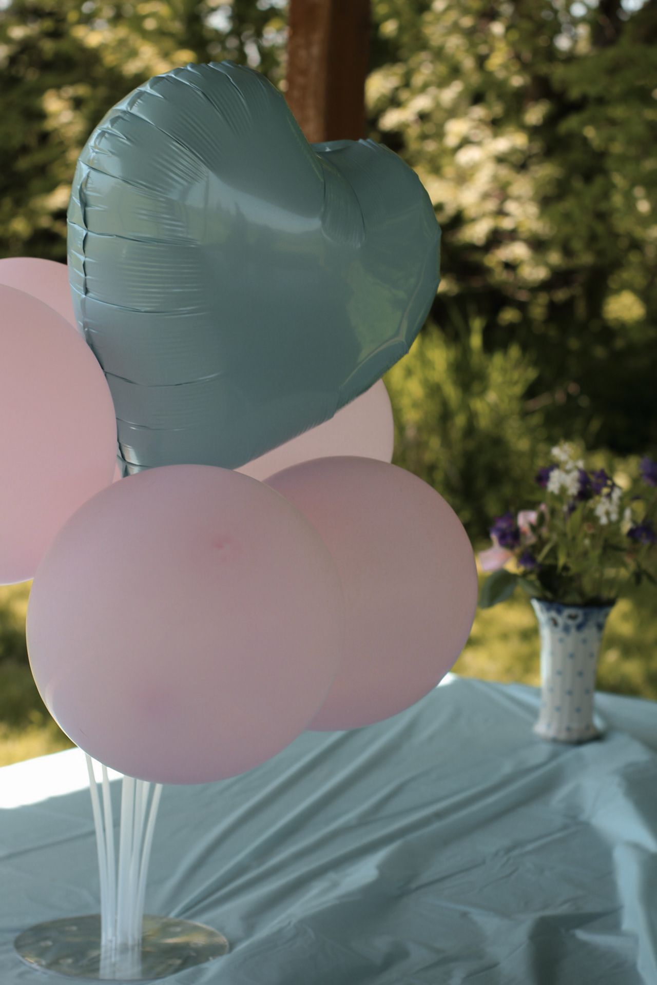 Pink and blue gender reveal party decorations arranged on a table outdoors with green foliage in background.