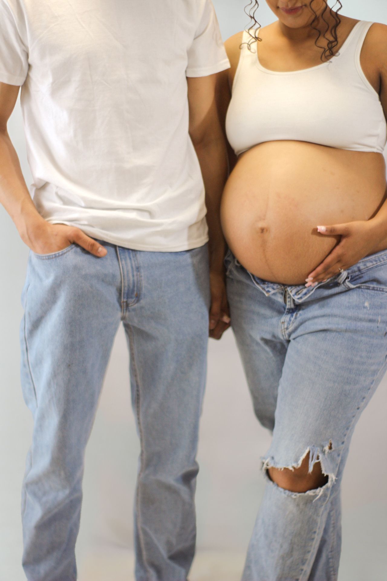 Cropped maternity photo showing couple in casual wear with visible baby bump.