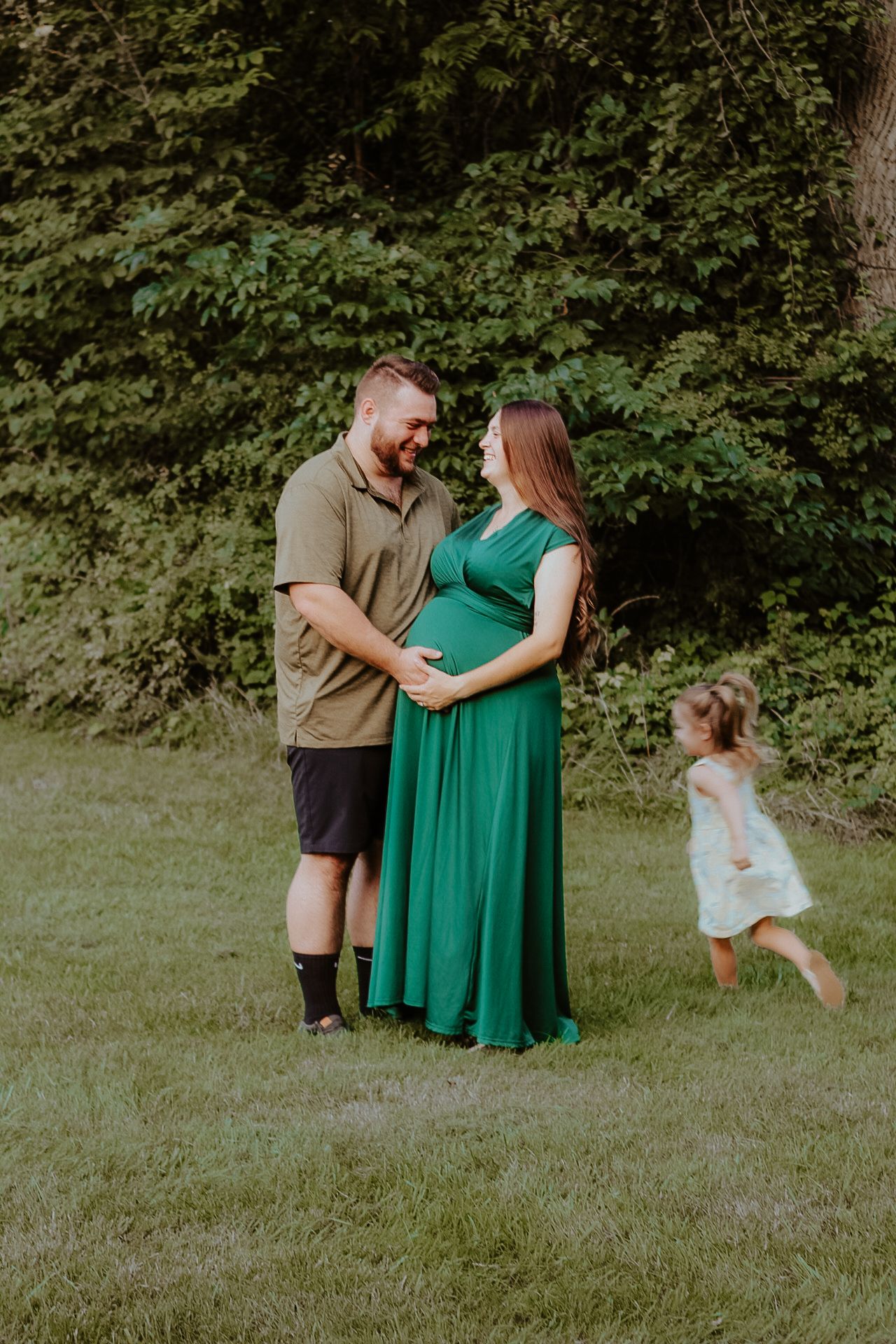 A family shares a tender moment in a green field during a maternity photoshoot.
