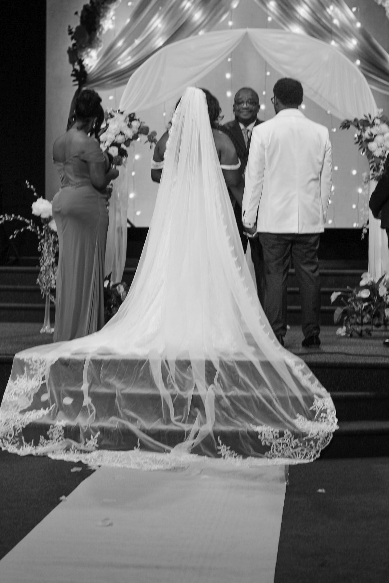 Wedding ceremony sequence showing dramatic train of lace wedding dress against lit backdrop.
